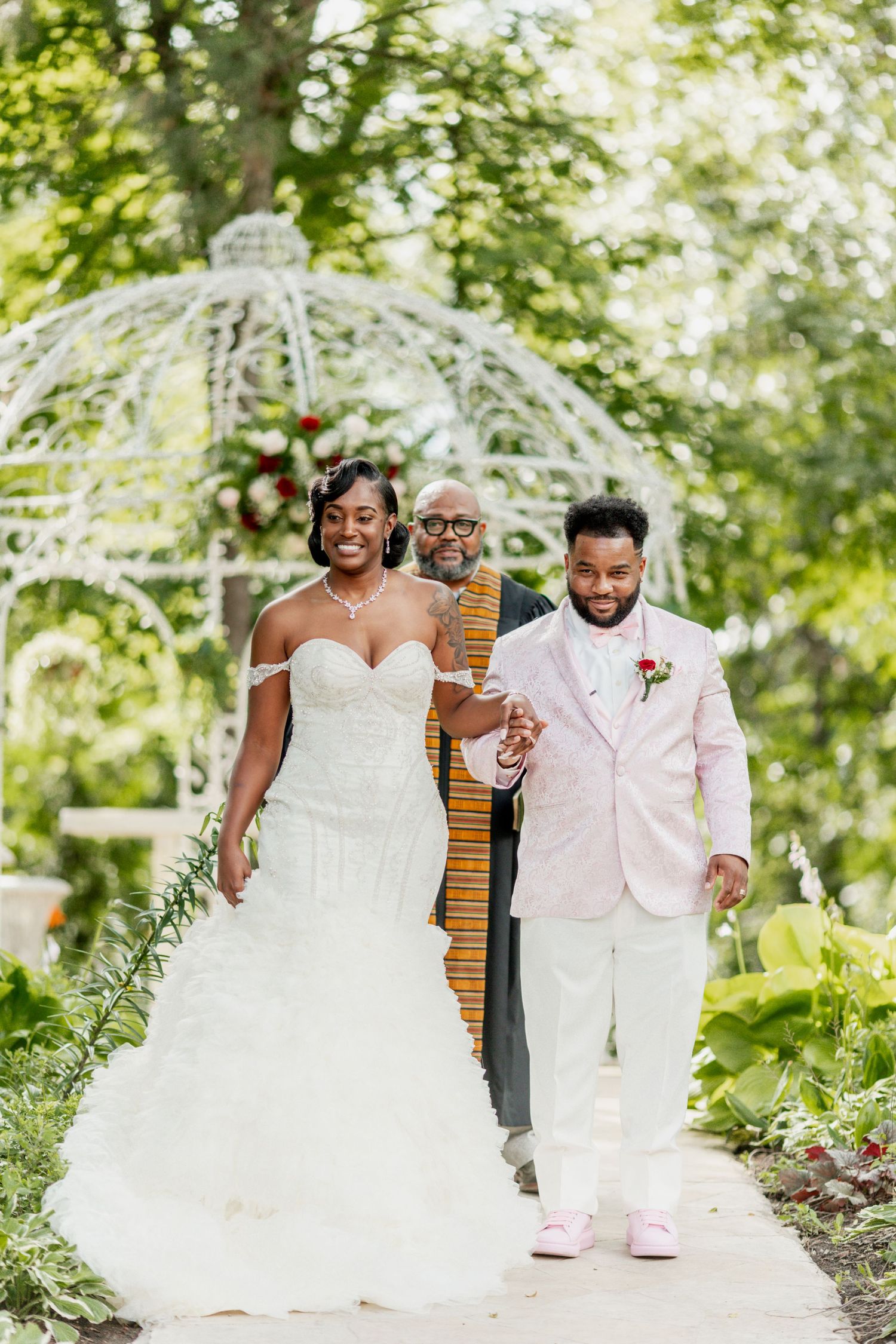 Happy couple poses with officiant under white garden gazebo after ceremony.