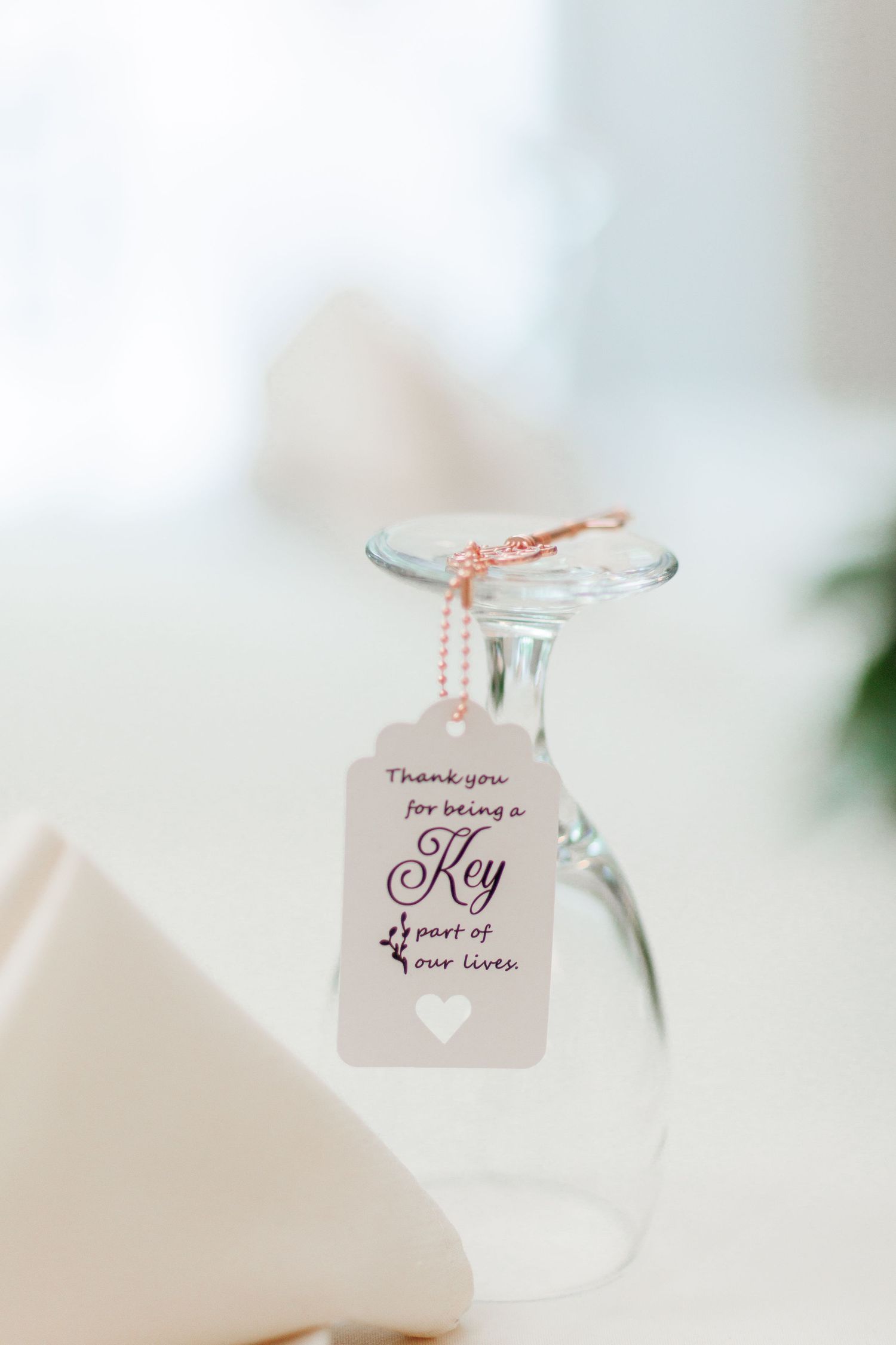 Wedding favor tag on wine glass reading Thank you for being a key part of our love.