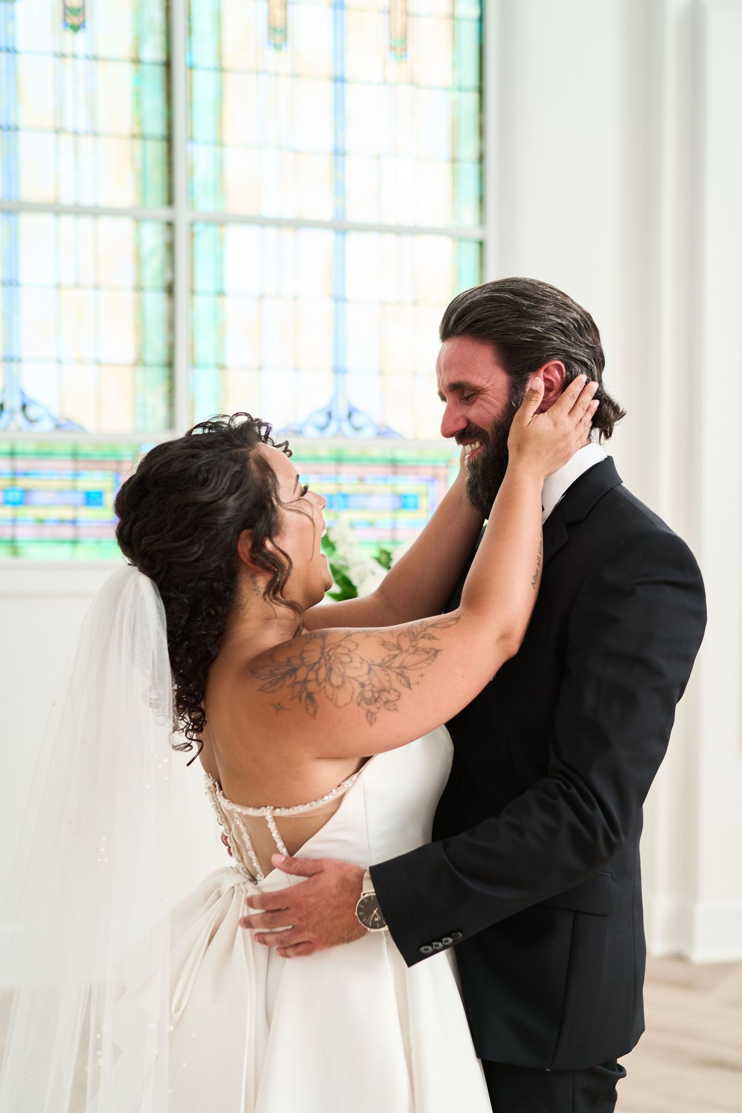 Intimate moment between newlyweds in front of stained glass windows during their wedding celebration.