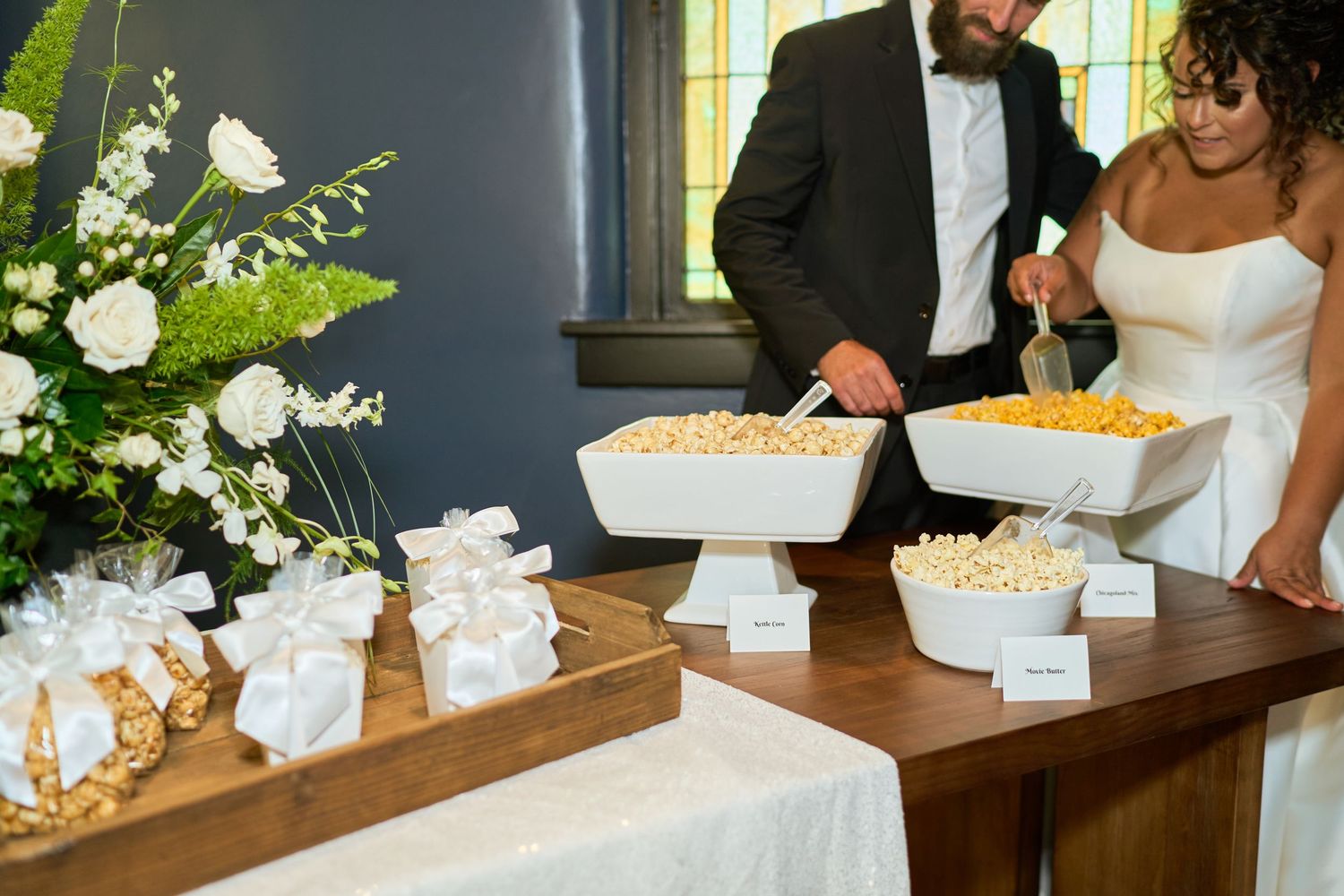 Wedding reception dessert table with white cake stands and popcorn bar setup.