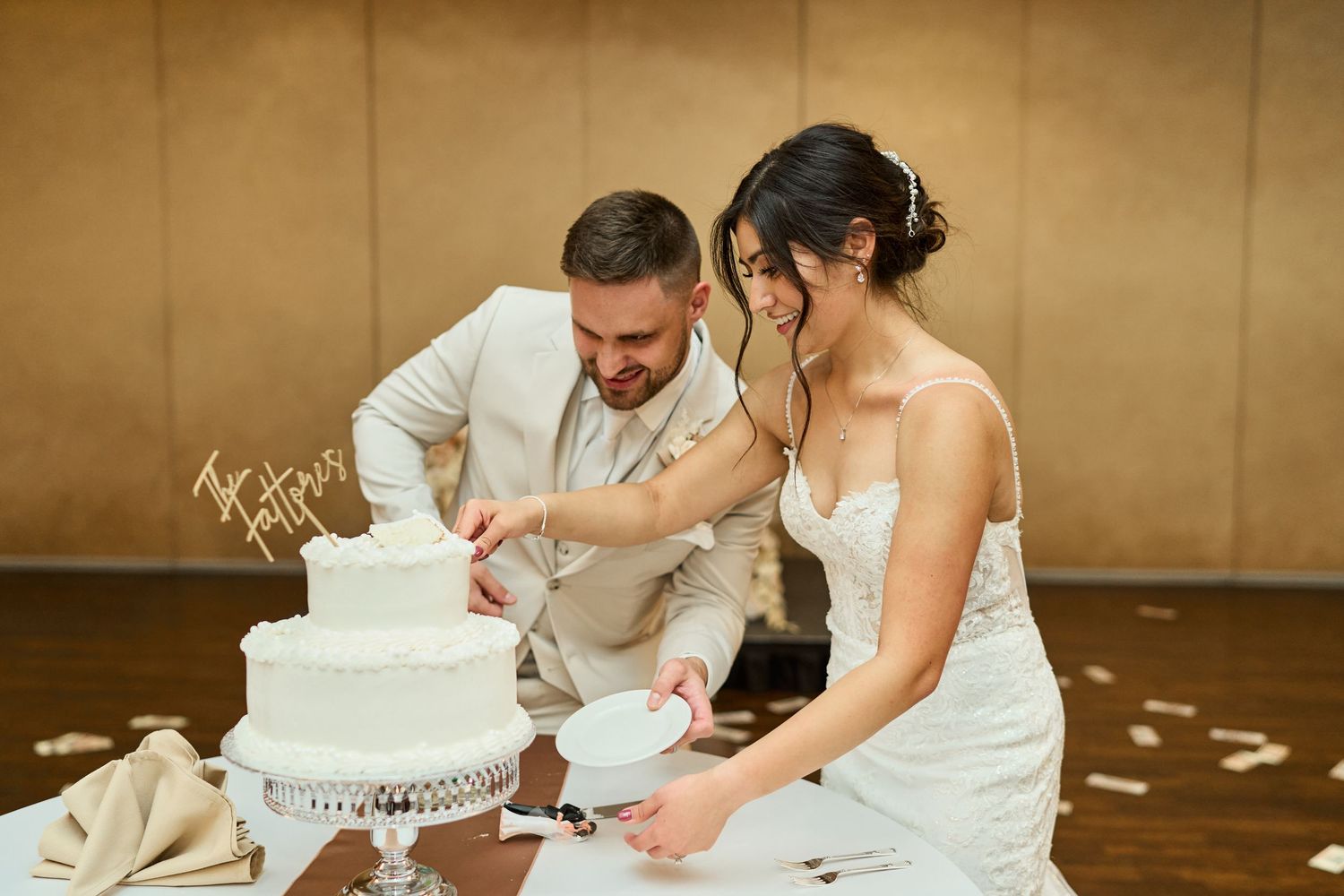A couple in formal wedding attire cuts into their white tiered wedding cake together.