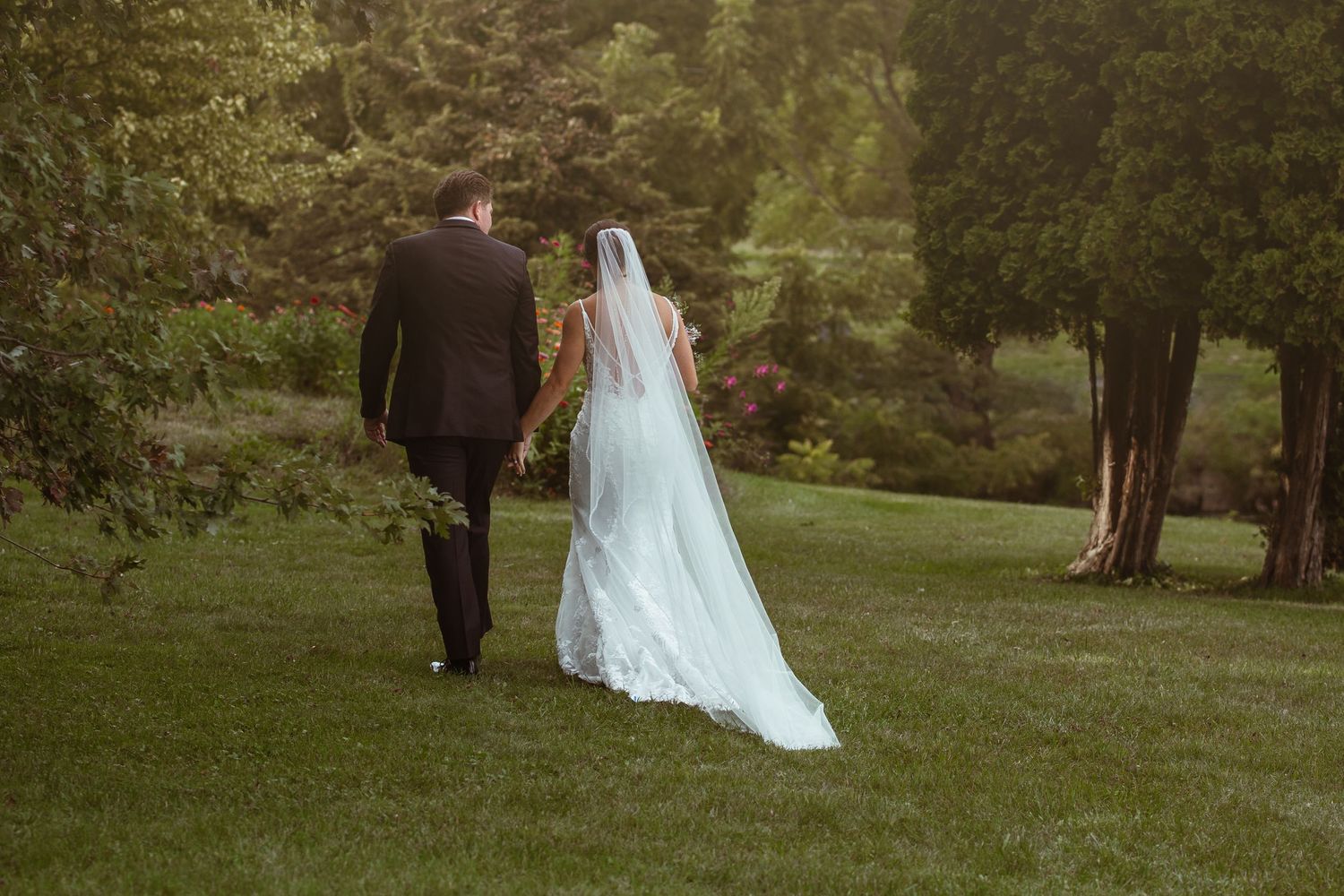 A couple walks together on a lush green lawn during a wedding celebration in an outdoor garden setting.