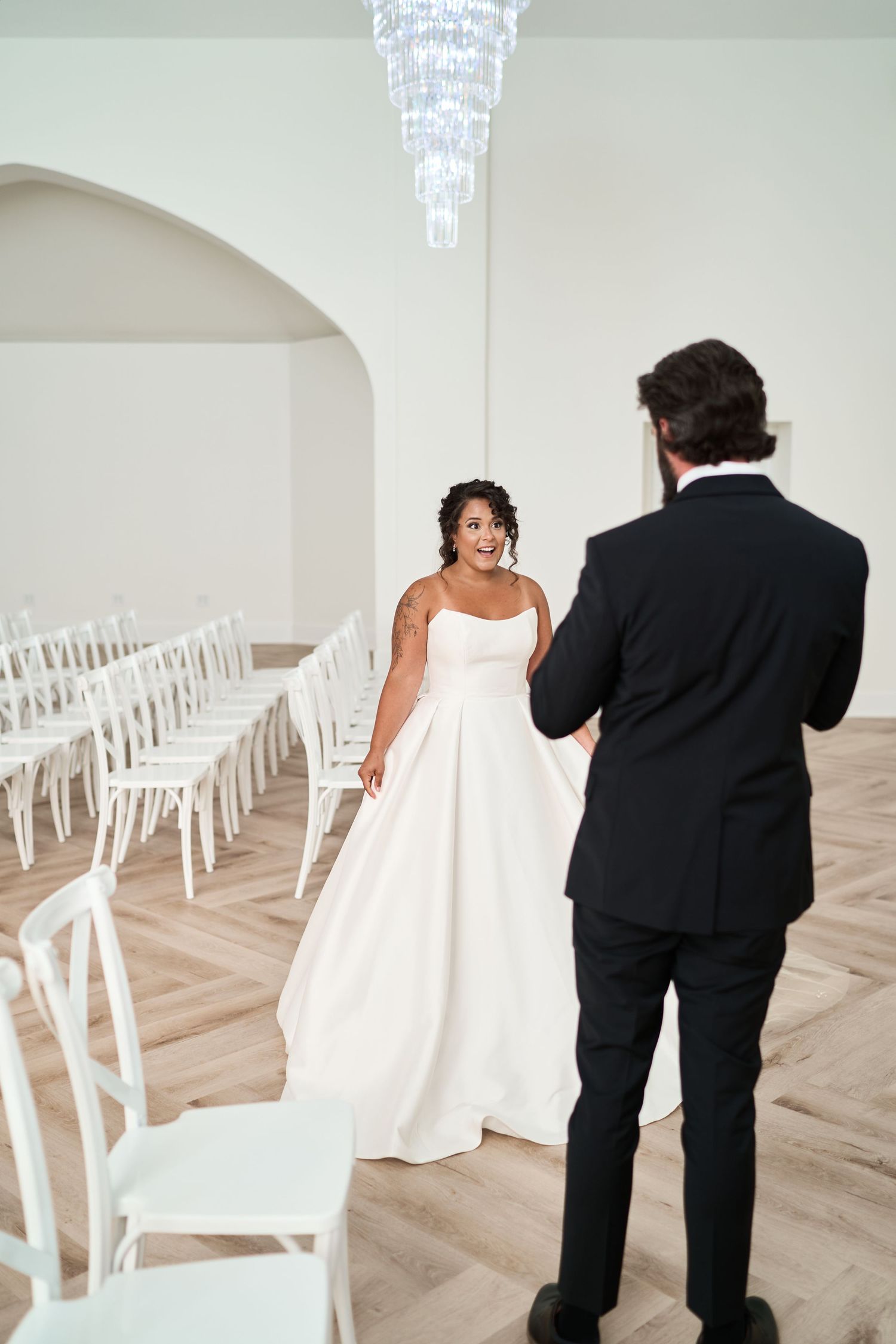 A modern chapel wedding venue with a crystal chandelier and white chairs arranged in rows.