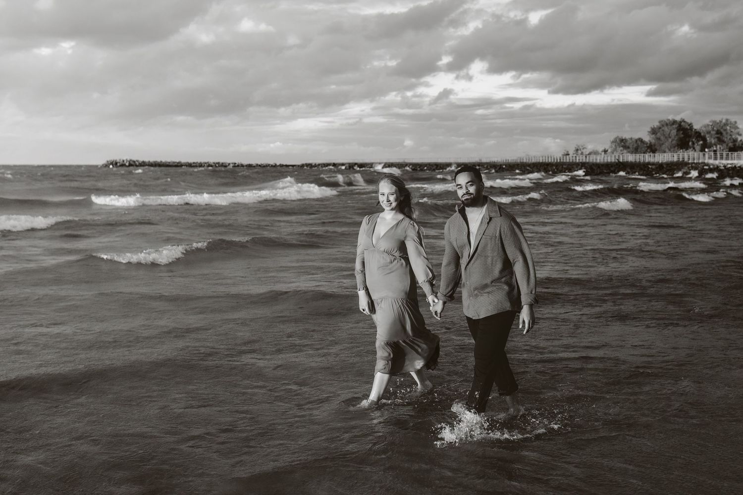 A couple walks together through gentle ocean waves along a scenic beach at sunset.