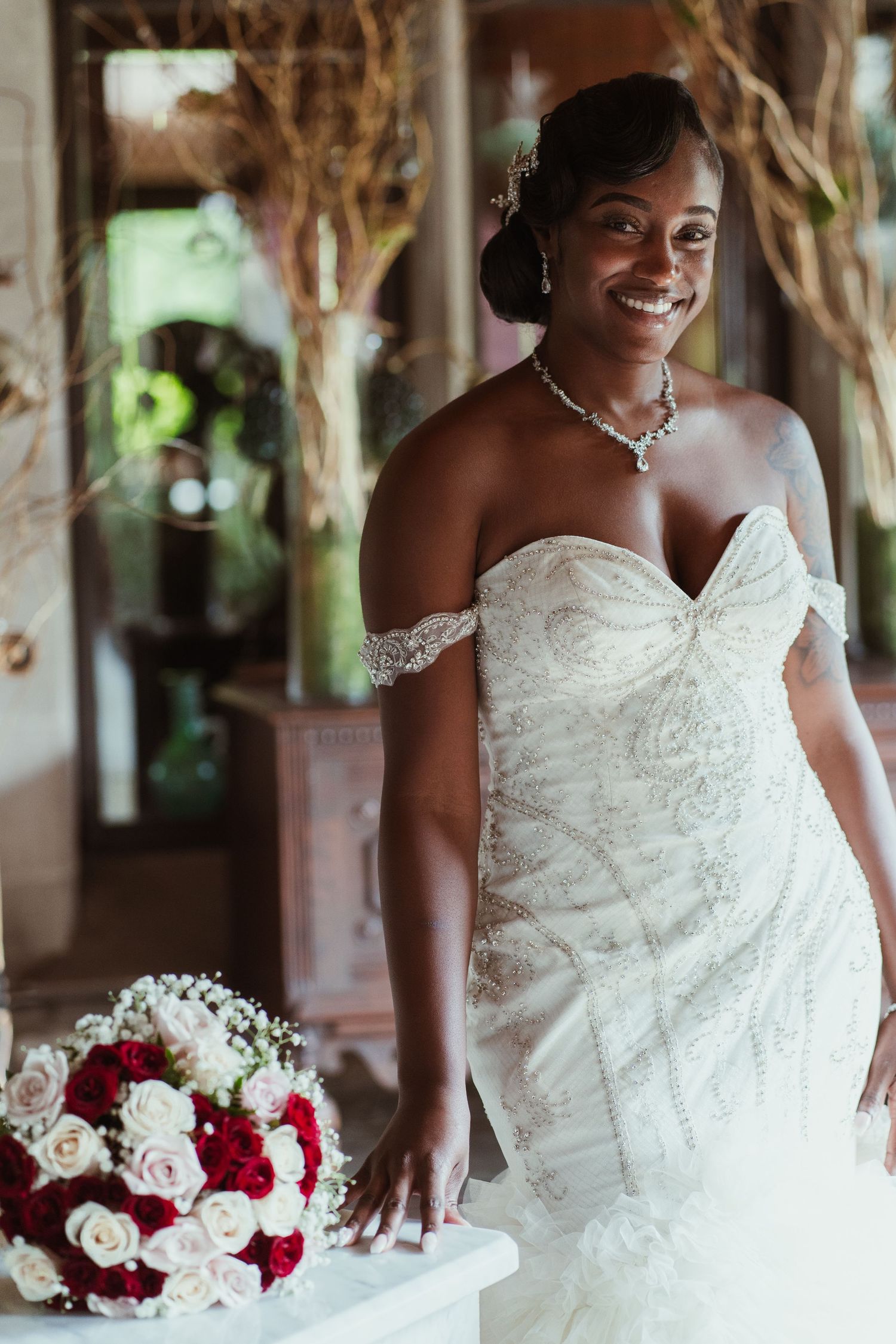 Bridal portrait featuring off-shoulder wedding gown and red rose bouquet in stone venue.