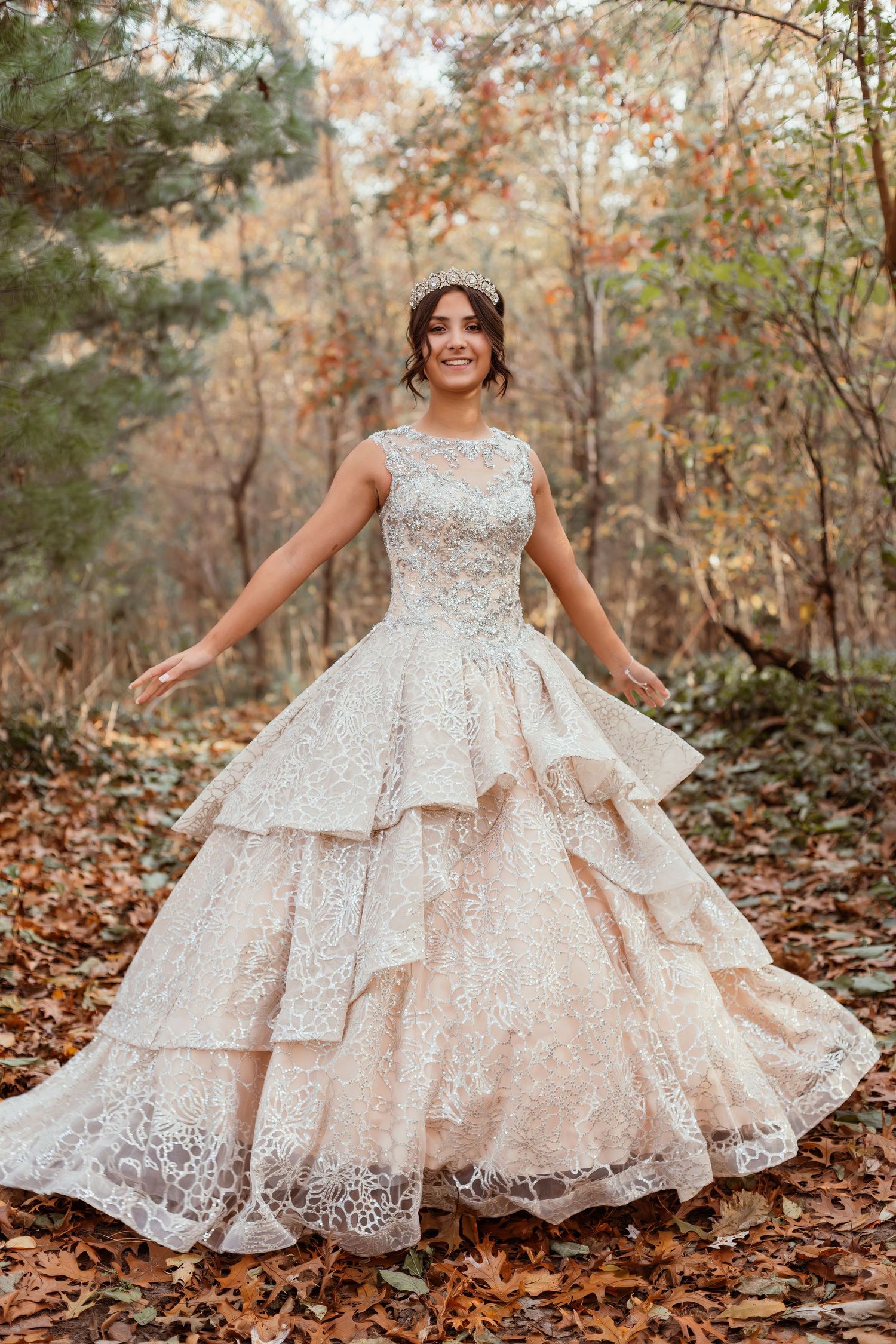 Elegant white lace wedding dress with tiered skirt shown twirling in fall forest.