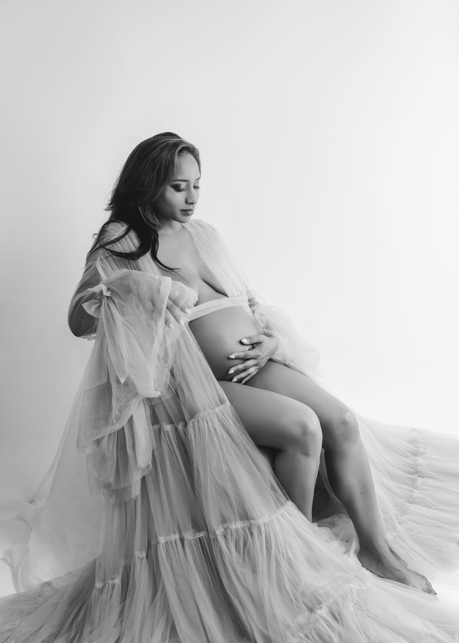 Black and white maternity photo of an expectant mother in a flowing sheer gown.