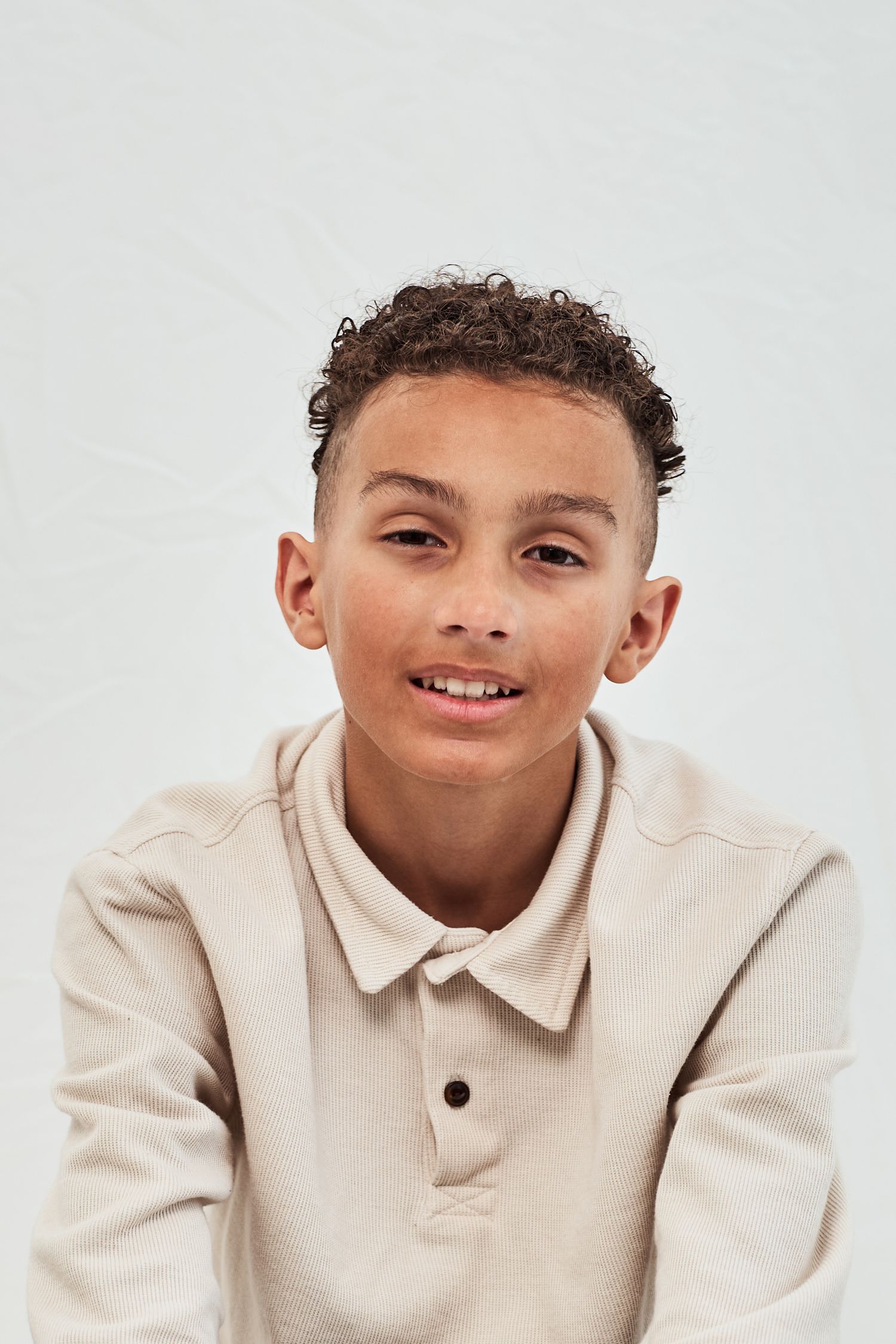 Young person wearing a beige polo sweater smiles warmly against a white background.