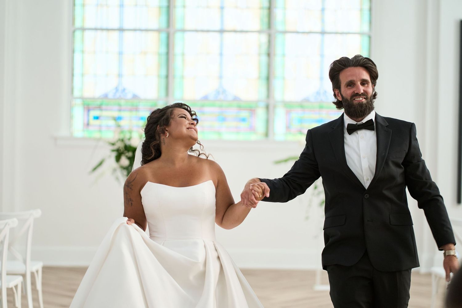 A joyful wedding celebration moment in a bright, airy chapel with stained glass windows.