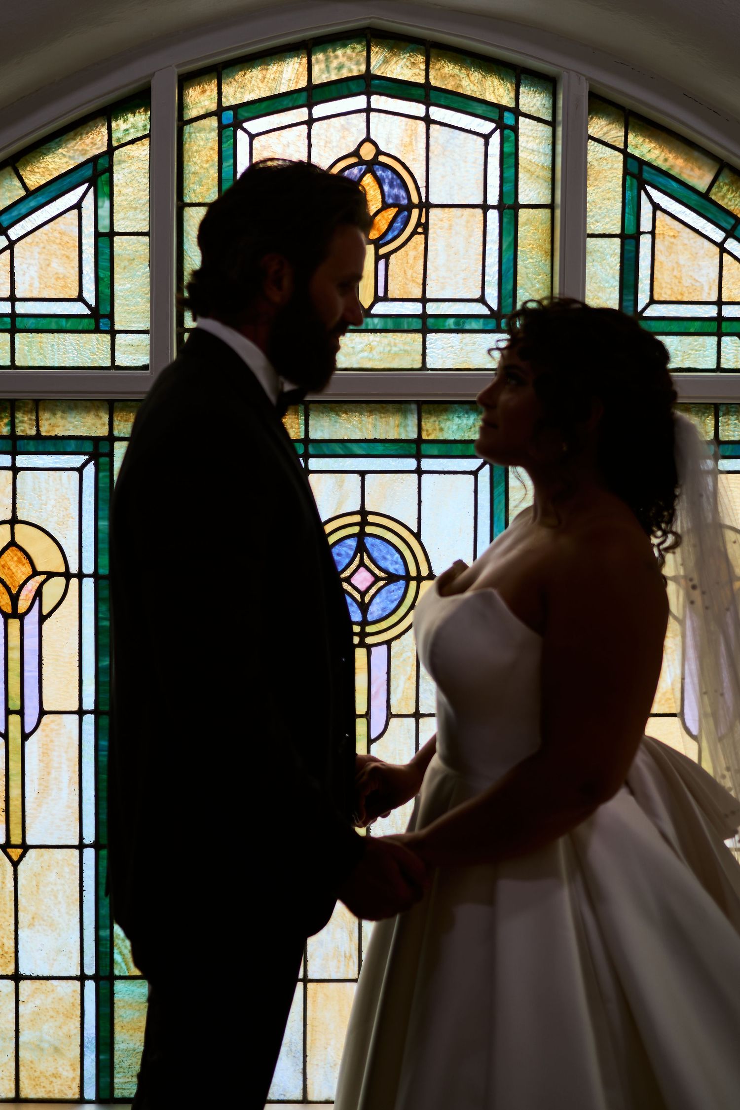 Silhouettes against stained glass windows showing dramatic wedding moment.