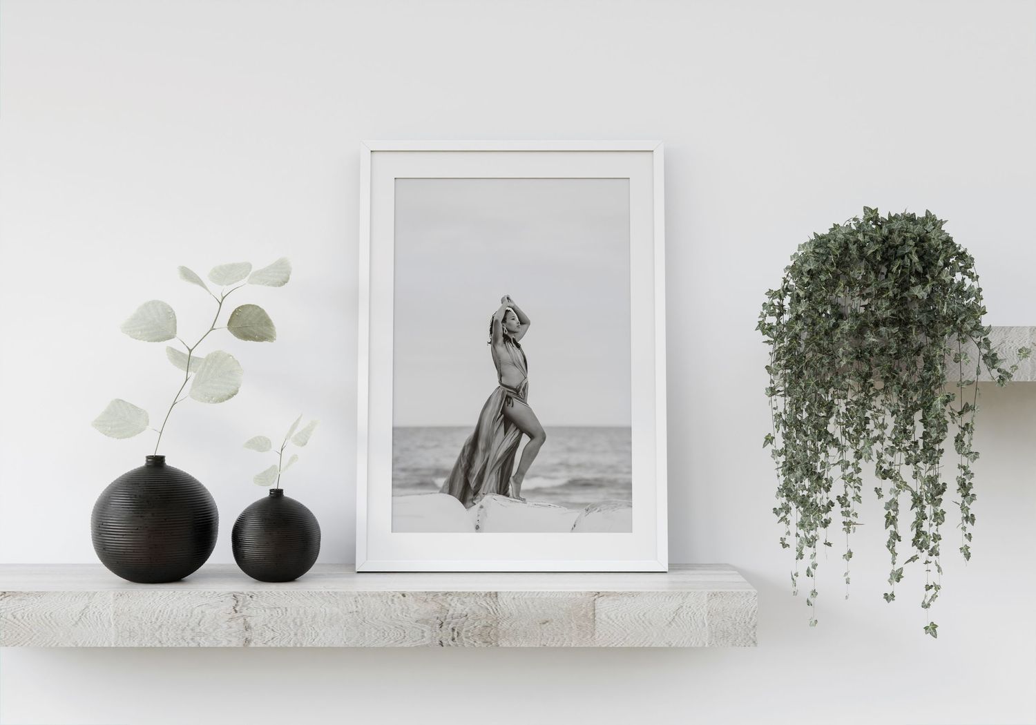 Minimalist white shelf display with black vases, framed black and white art, and trailing plants.
