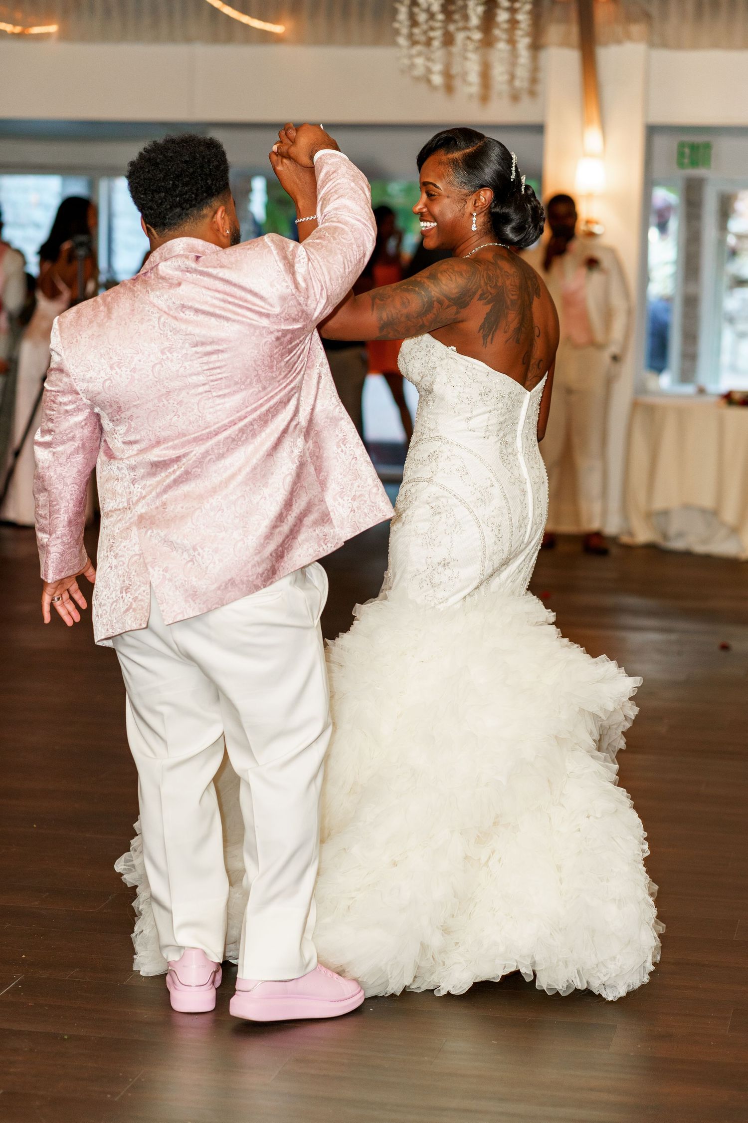 Couple dancing at a wedding reception with the bride wearing a white mermaid gown and the groom in pink and white attire.