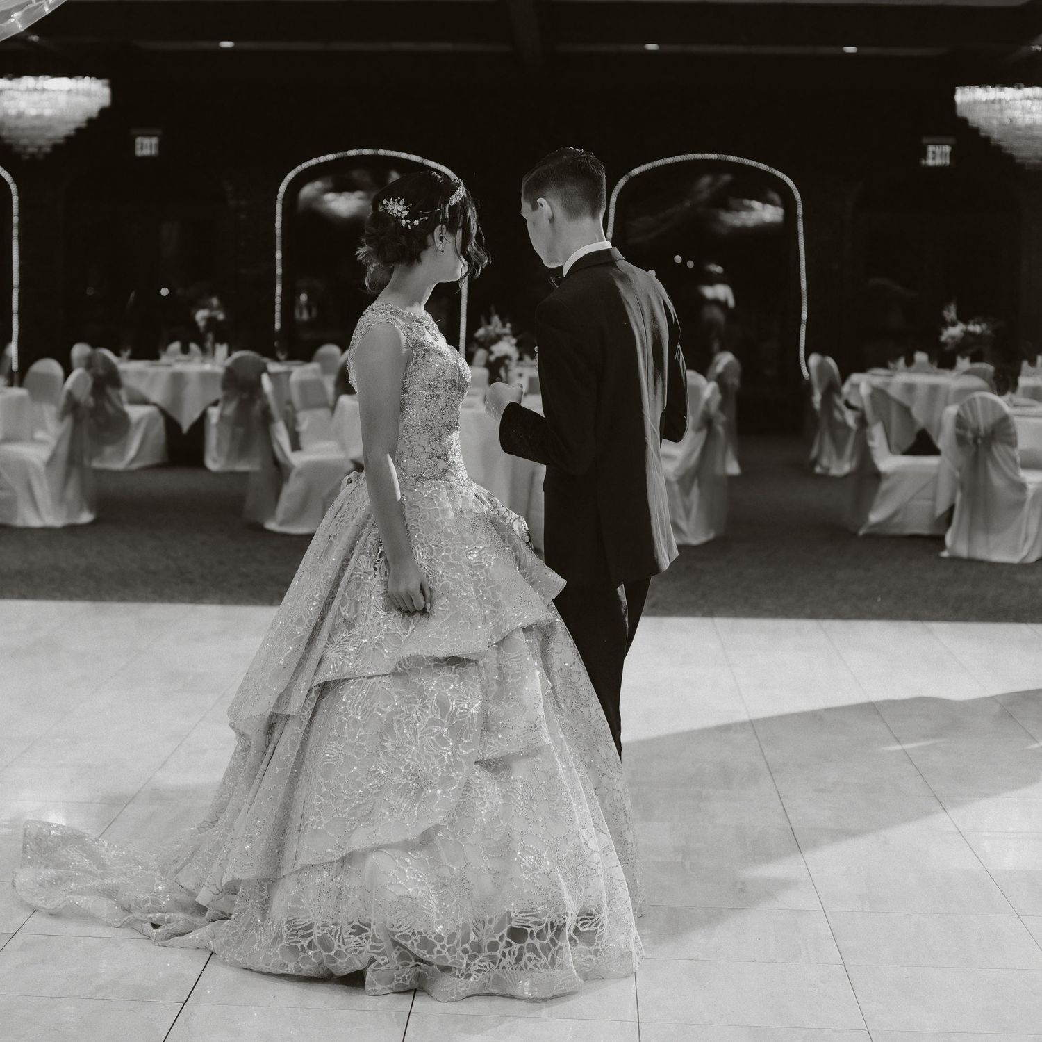 A couple dancing in formal attire at an elegant ballroom decorated with white chair covers.