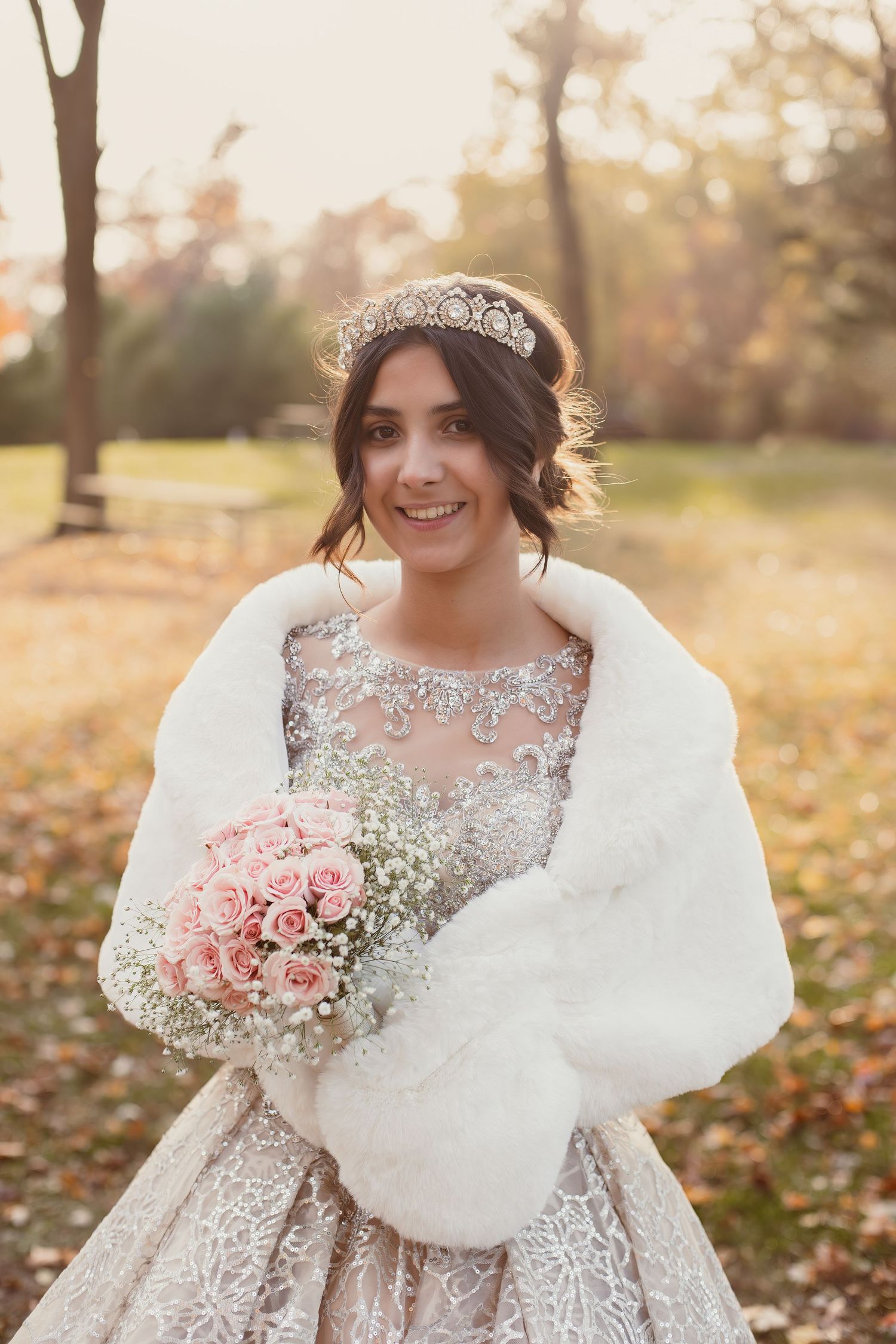 Bridal portrait with white fur wrap and pink rose bouquet in autumn setting.