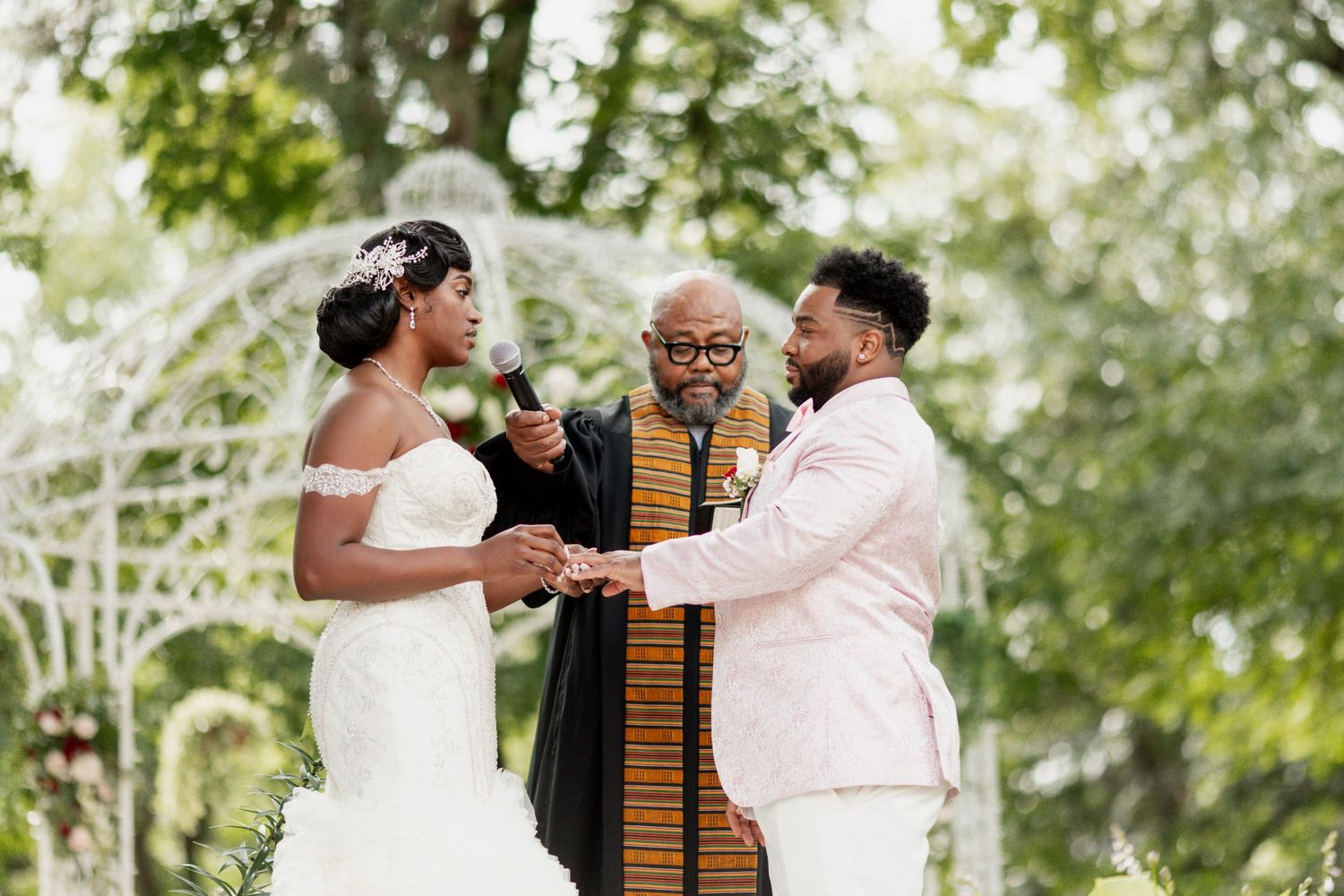 Intimate outdoor wedding ceremony under decorative white gazebo.