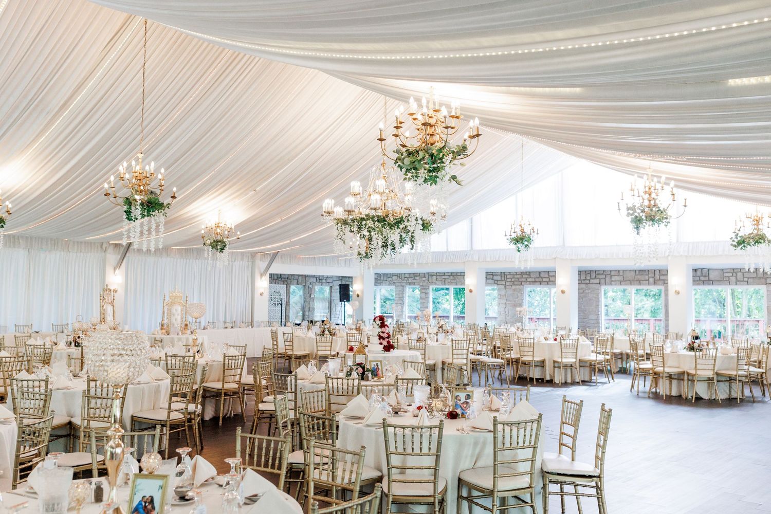 Elegant white wedding reception venue with draped ceiling, chandeliers and chiavari chairs.
