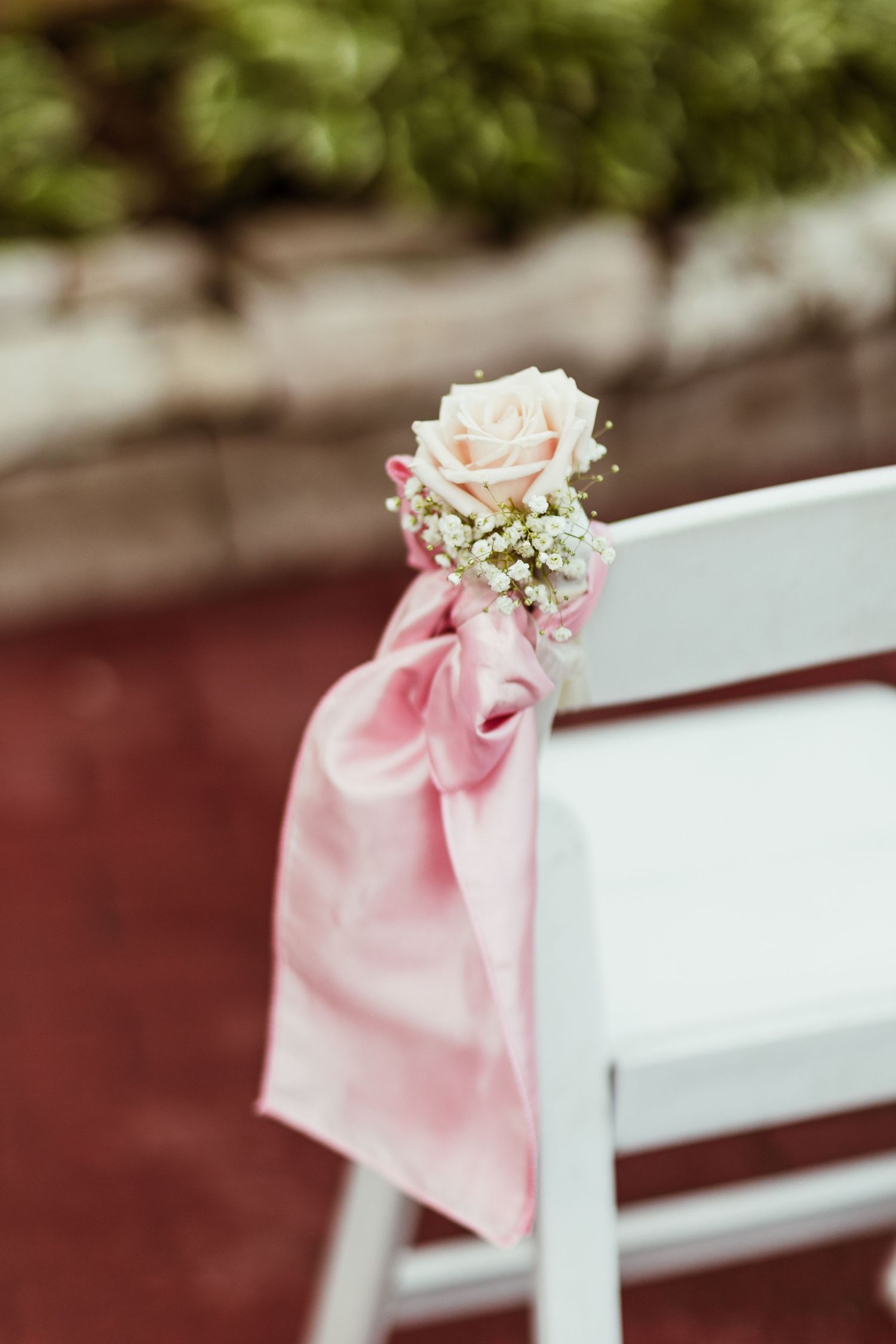 A white folding chair decorated with pink satin bow and pale rose for wedding ceremony.