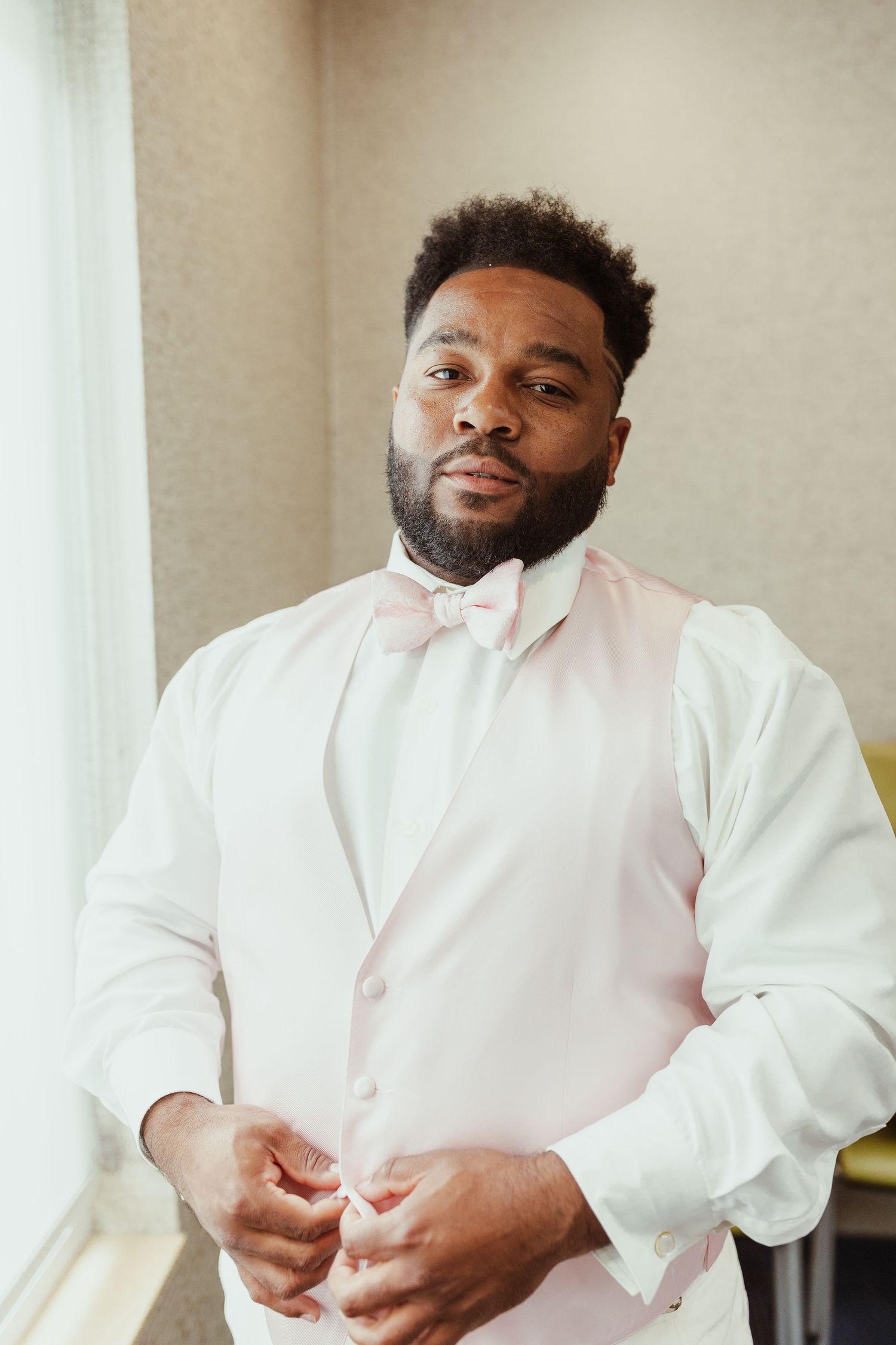 Person in white dress shirt and pink bow tie adjusting formal attire.