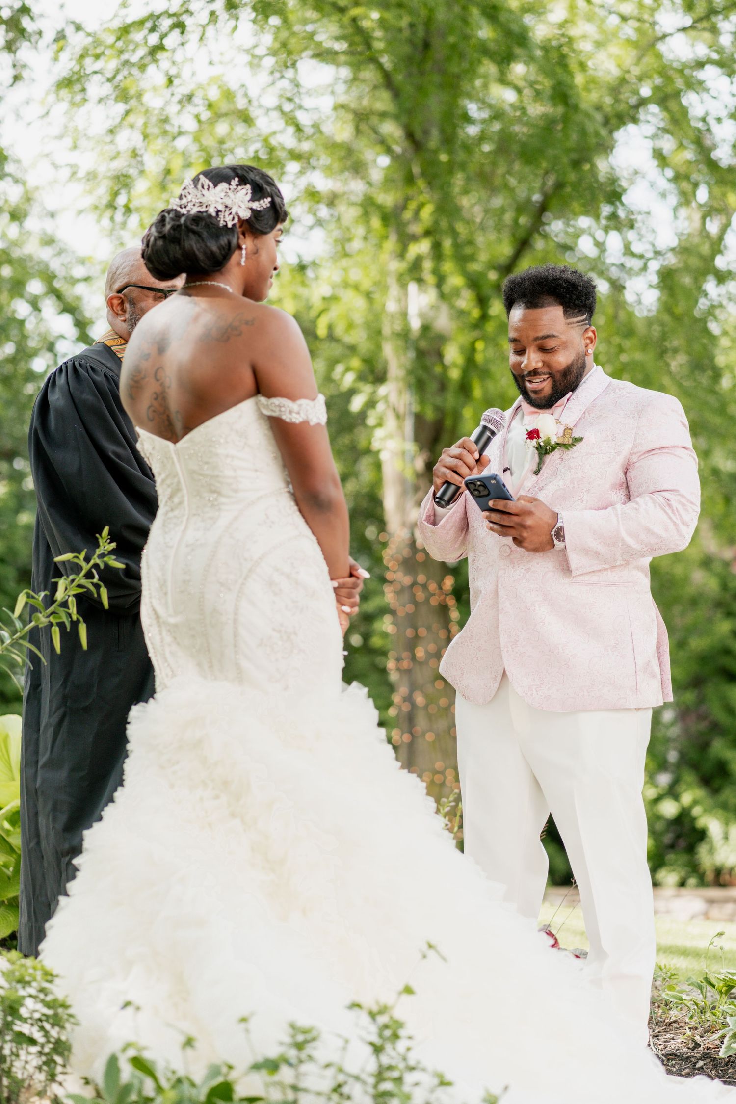 A couple exchanges vows during an outdoor wedding ceremony with the bride in white and groom in pink.