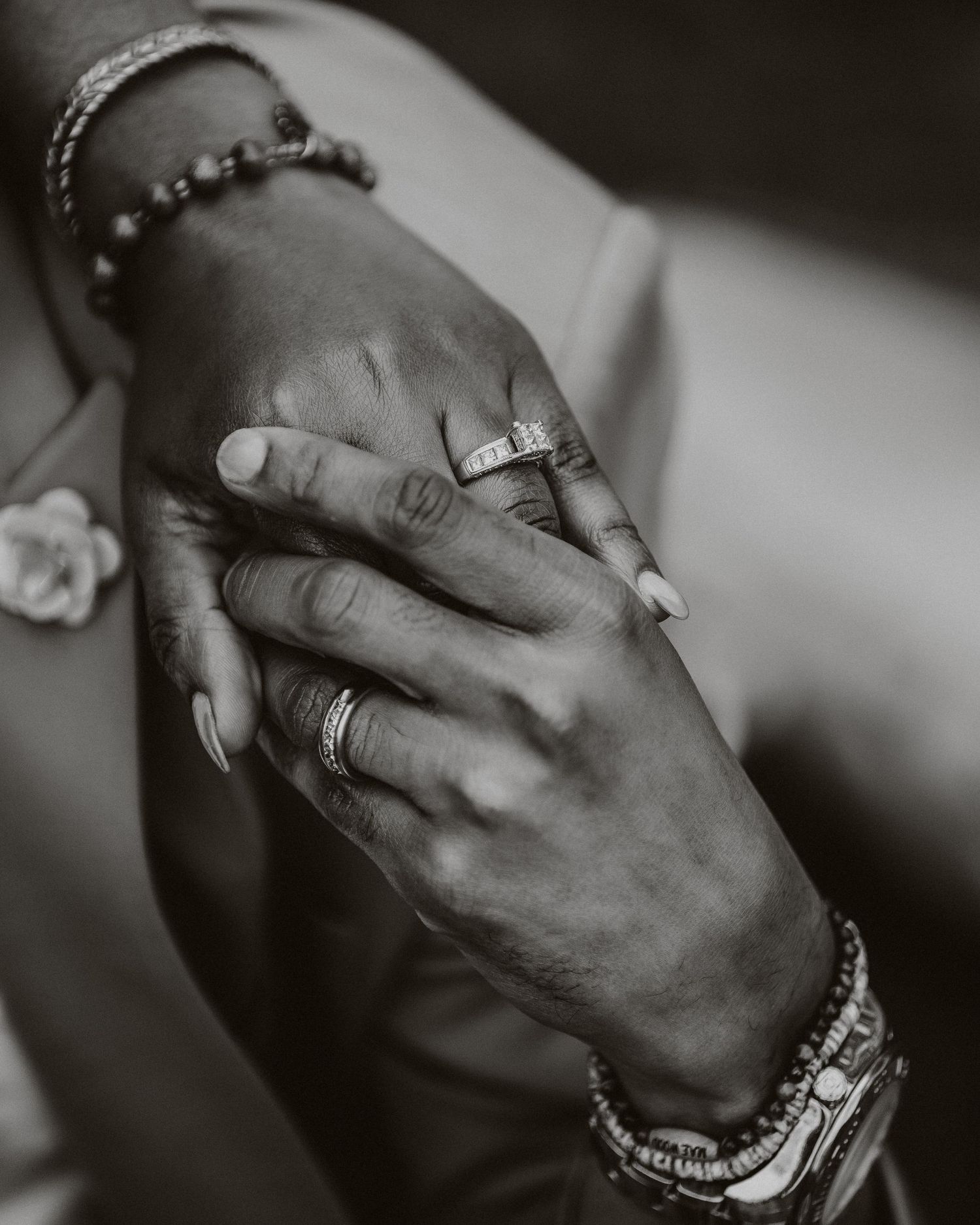 Close-up of hands with jewelry and rings touching intimately in black and white.