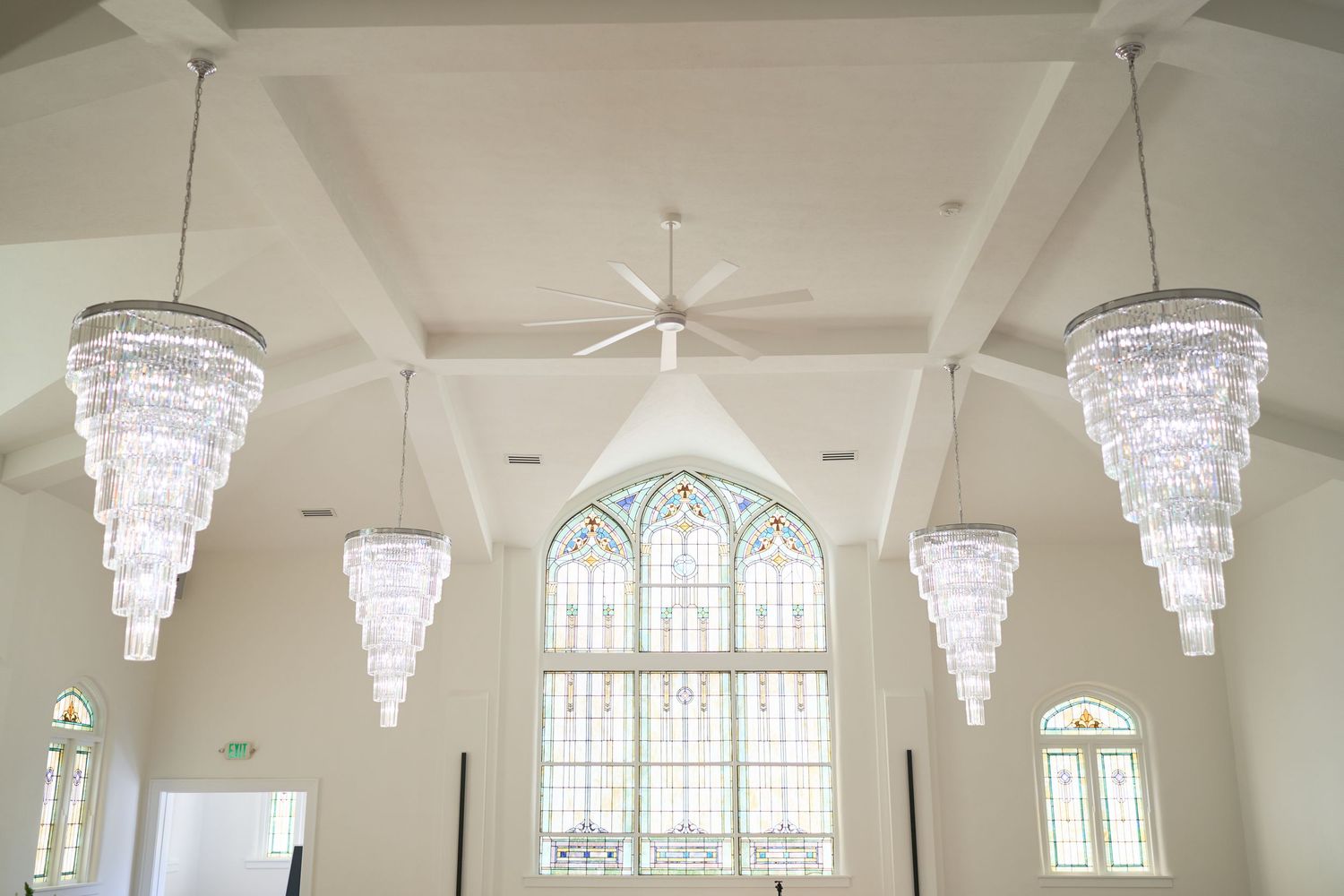 Elegant crystal chandeliers hang from vaulted ceiling with stained glass church windows.