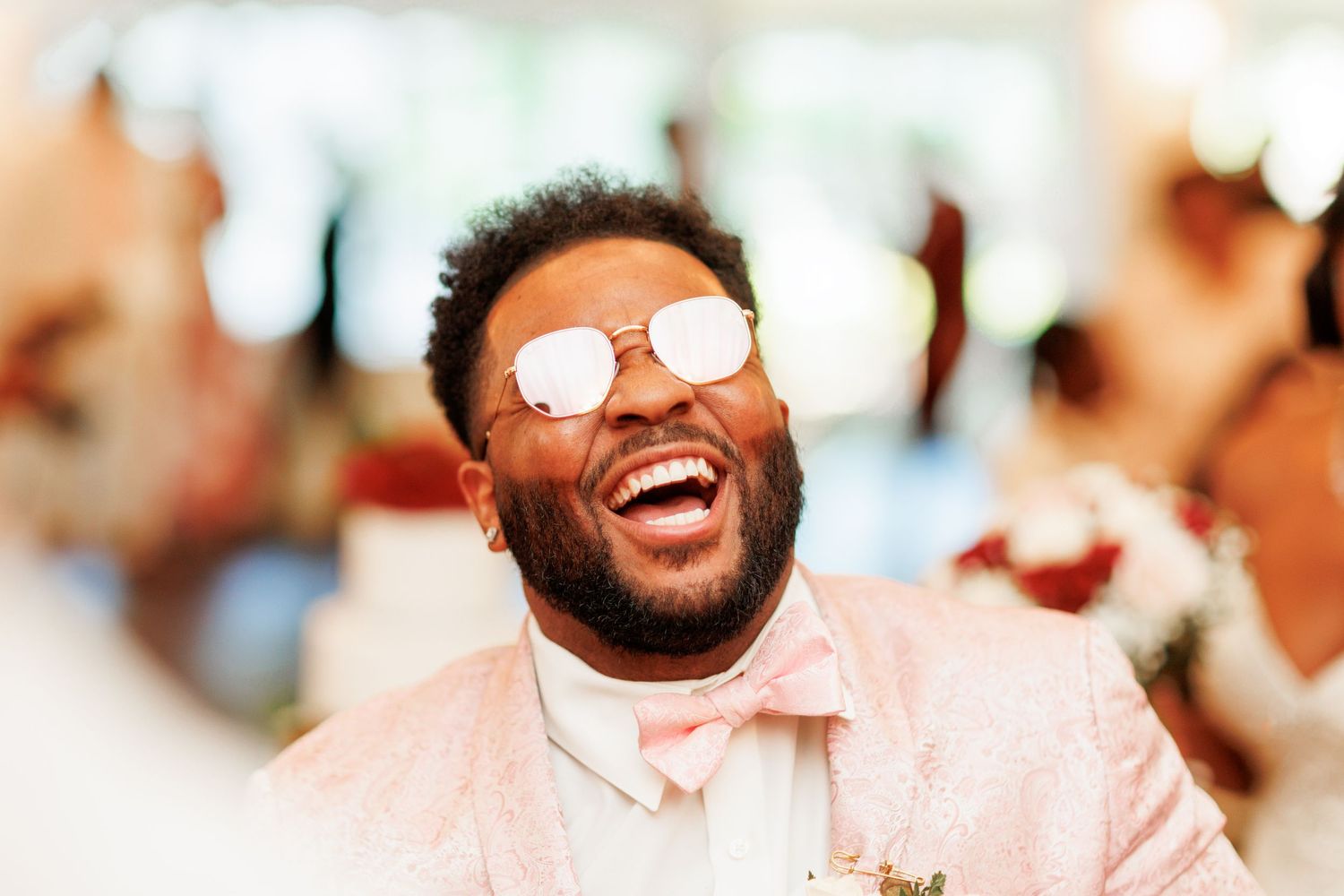 Wedding guest in pink suit and sunglasses smiles with pure joy during the celebration.