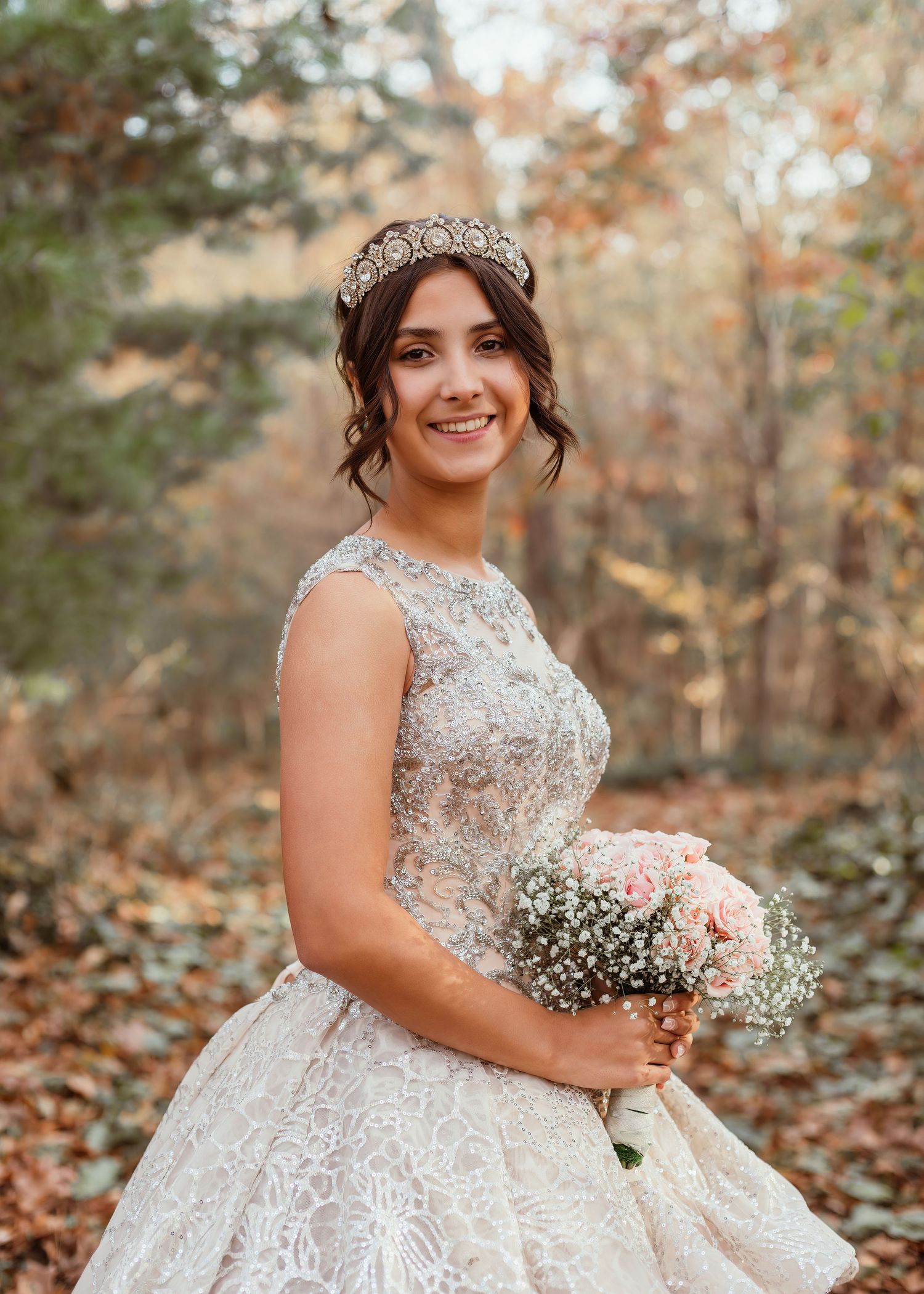 Ethereal bridal portrait showcasing a beaded ball gown and delicate bouquet in autumn woods.