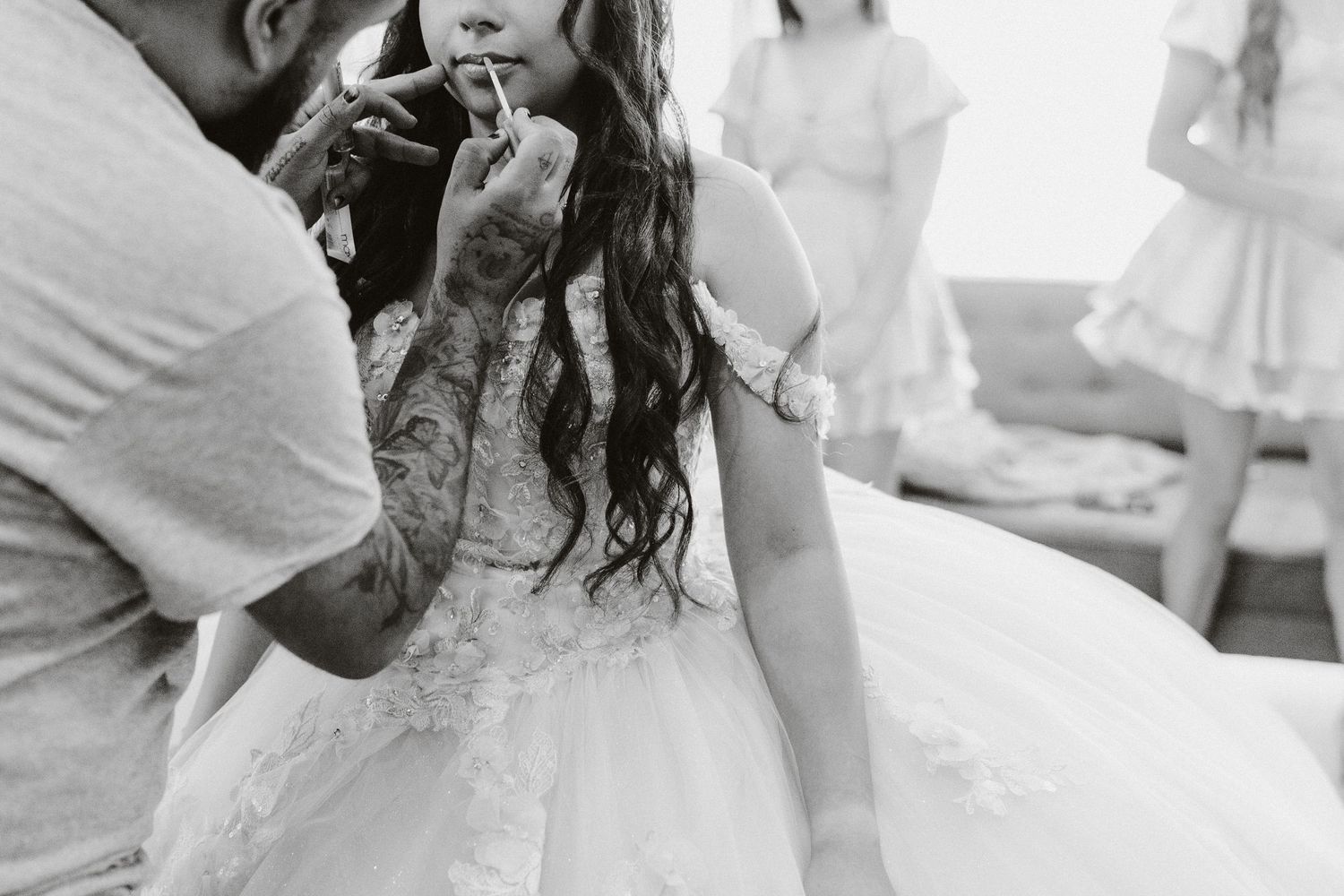 A black and white photo of final makeup touches being applied to someone in a wedding dress.