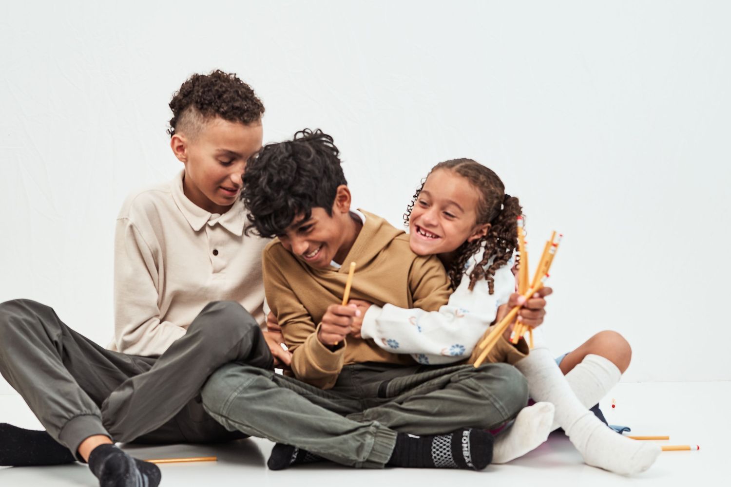 A group of joyful people in coordinated brown and gray outfits pose playfully together for studio photos.