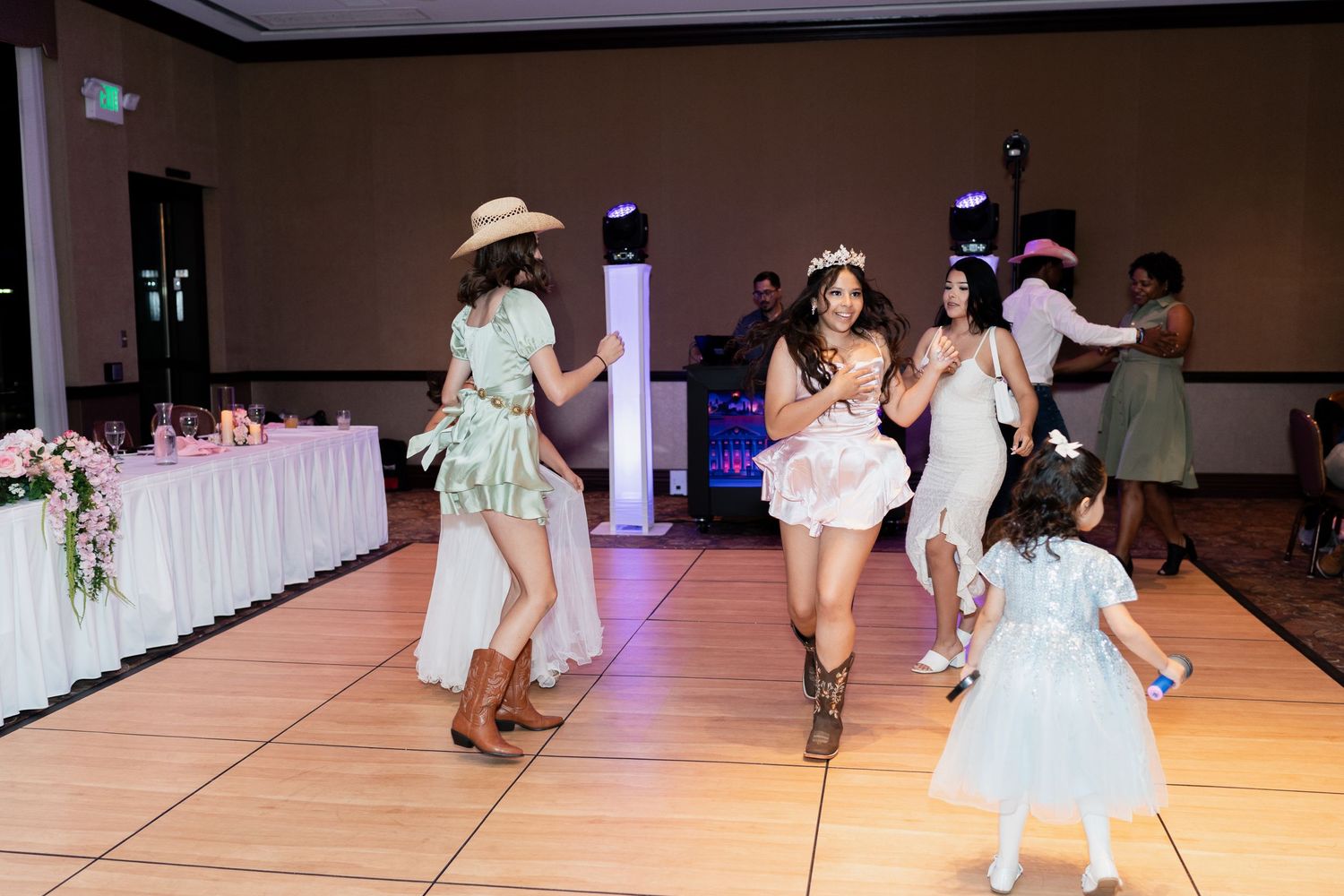 People dancing together on a lit dance floor at a reception with a decorated white table in the background.