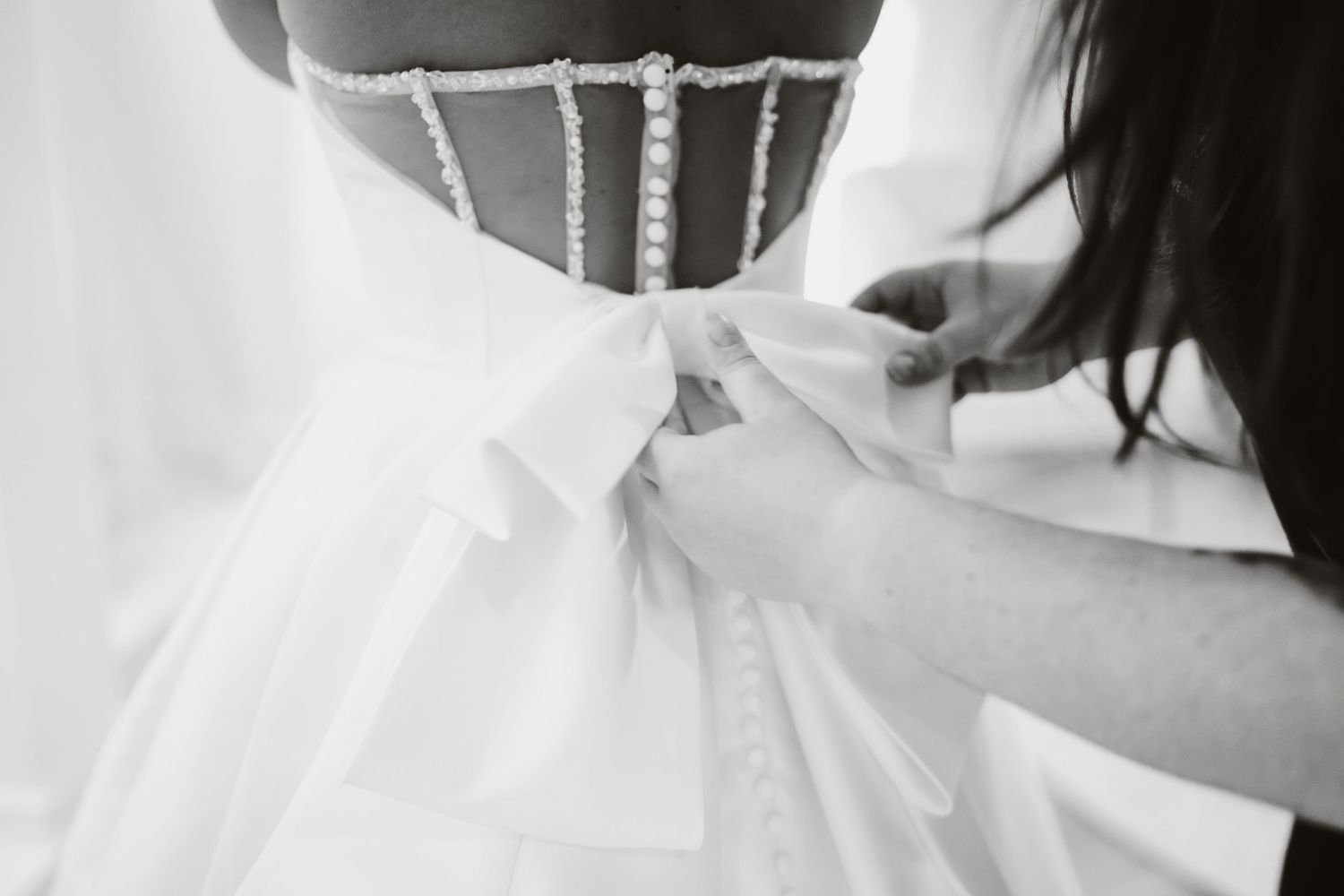 Close-up black and white shot of a wedding dress bodice being fastened.