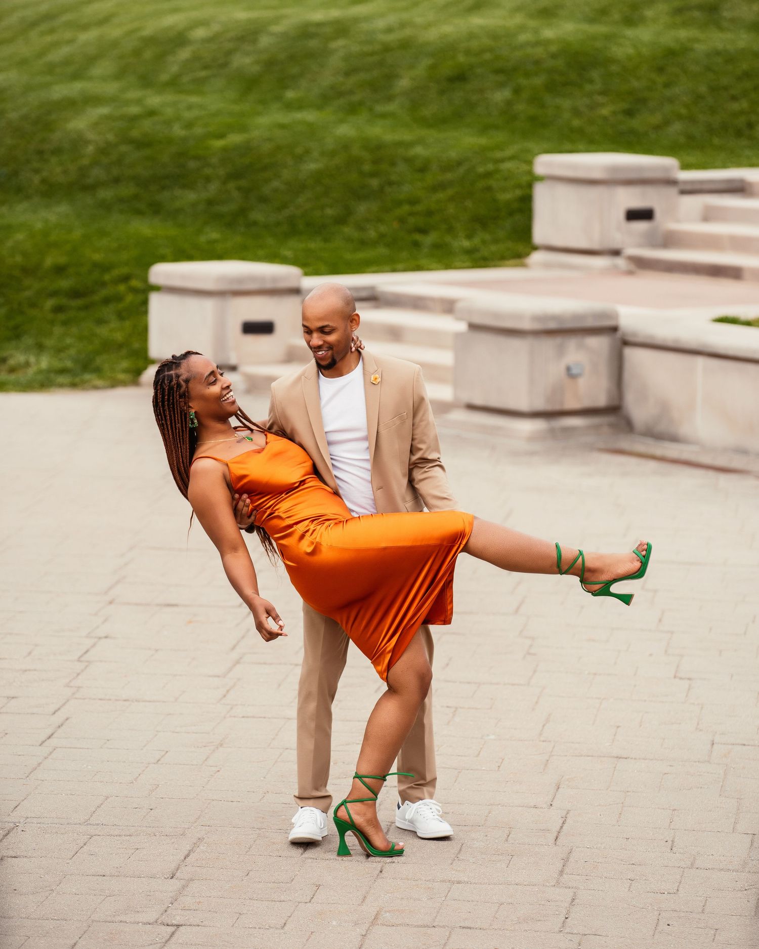 A couple enjoying a playful moment outdoors, with the woman in an orange dress striking a fun pose.