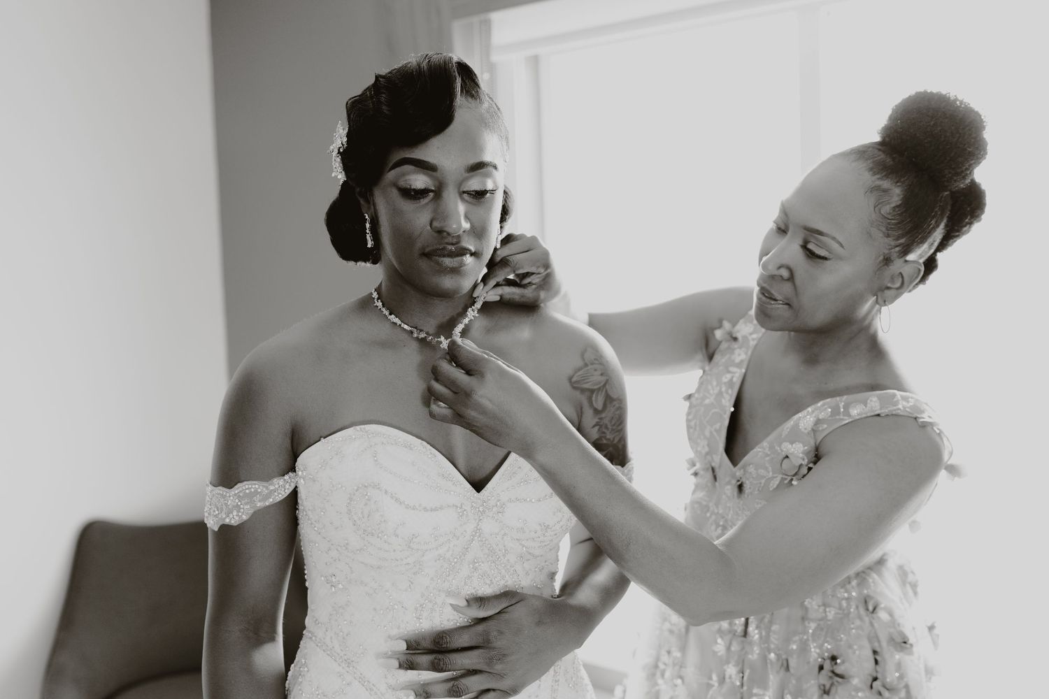 A tender moment during wedding preparations in black and white as finishing touches are added to a strapless gown.