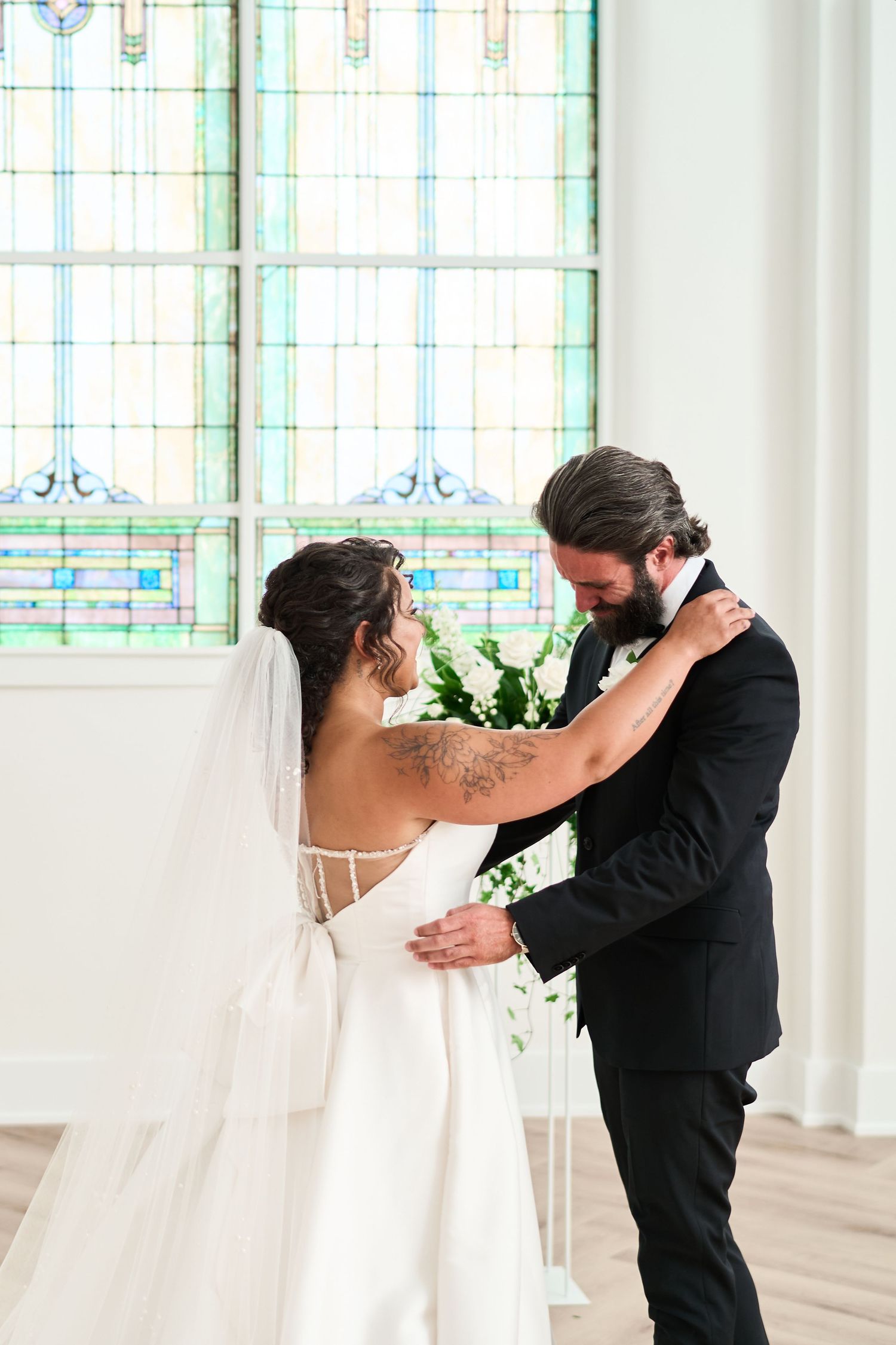 Romantic first-look moment in a light-filled chapel with elegant stained glass windows.