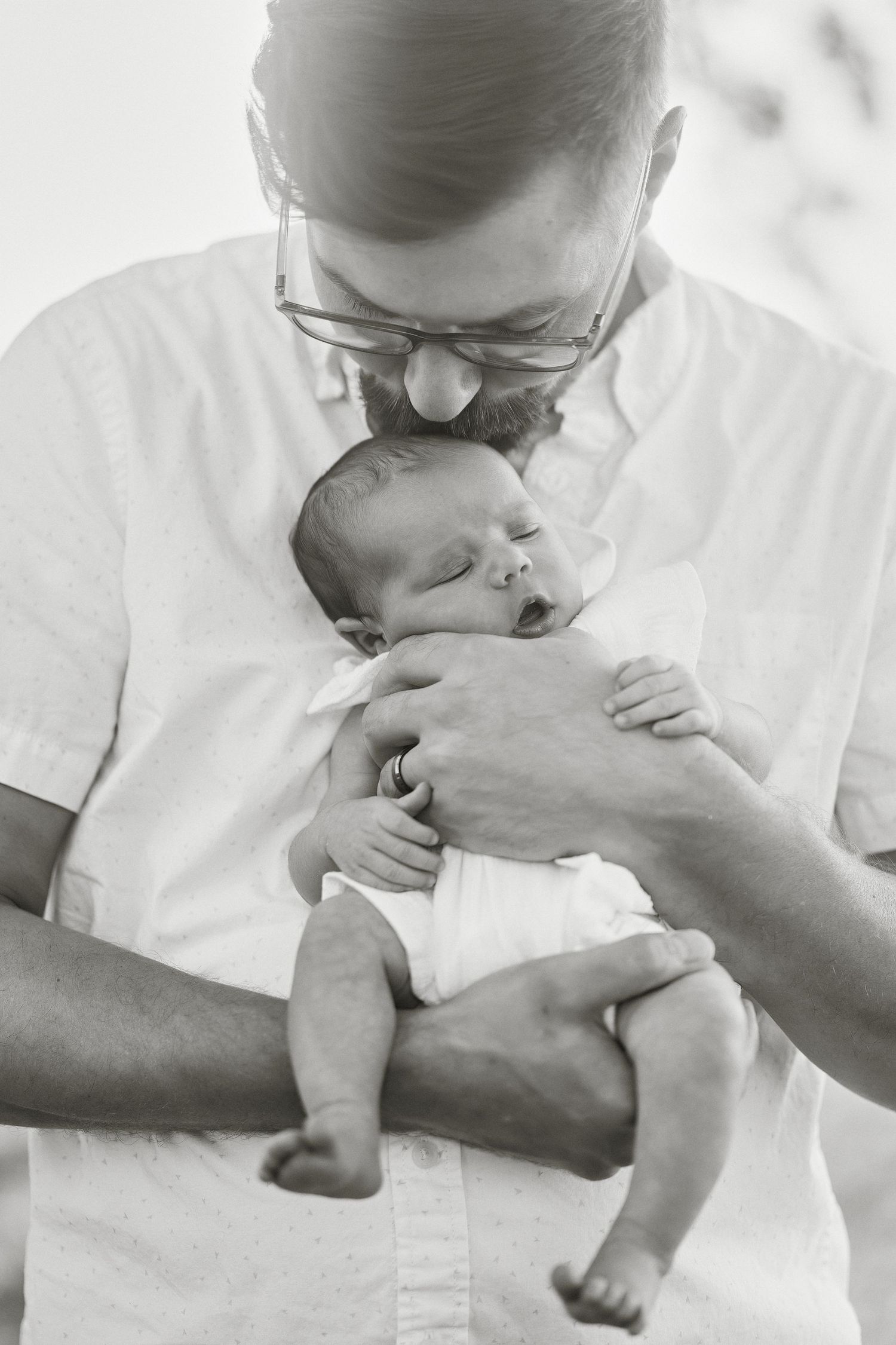 Black and white photo series showing tender moments between a parent and baby in matching white outfits.