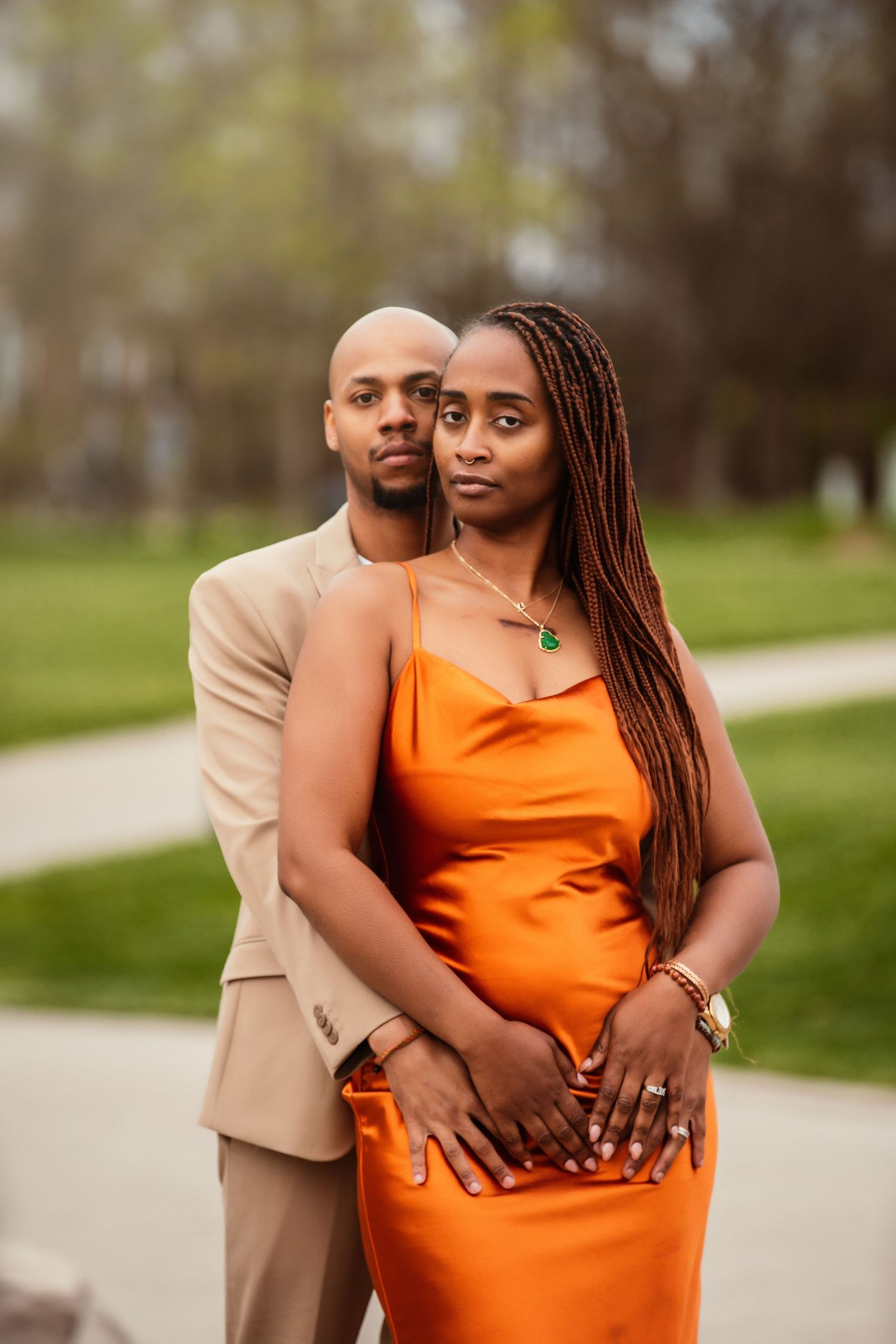 A couple in coordinated formal attire pose together outdoors against a green backdrop.
