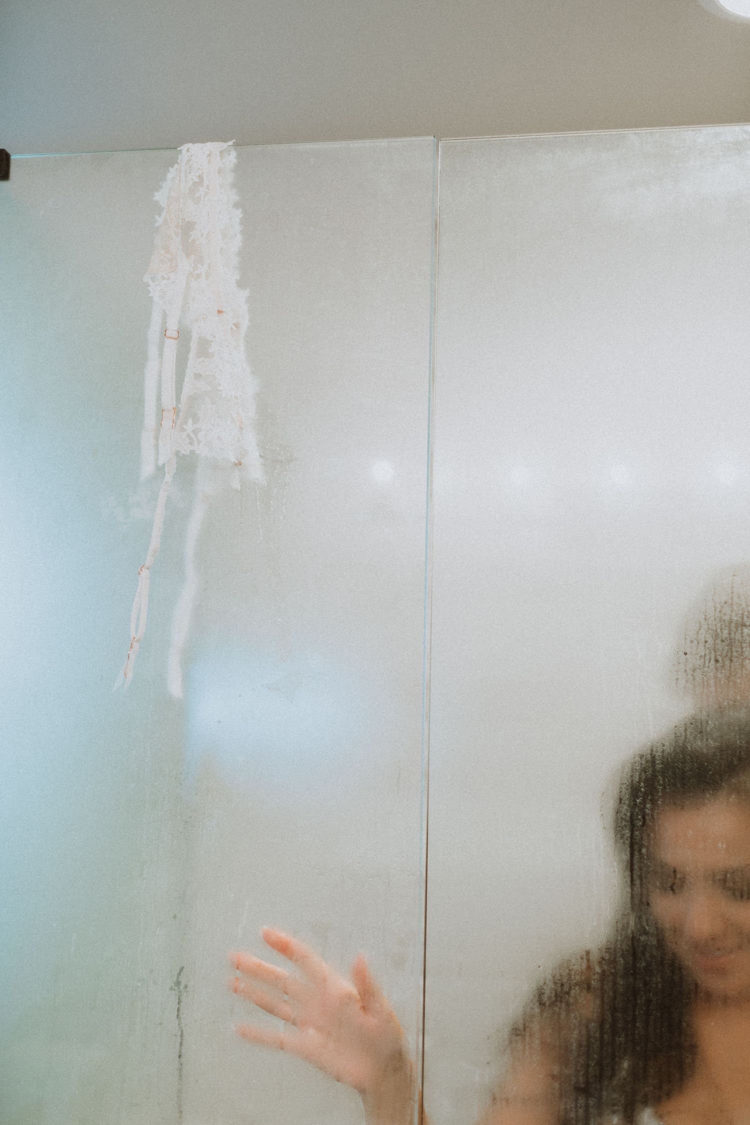 A blurred figure behind a steamy shower glass with a mark or smudge visible.