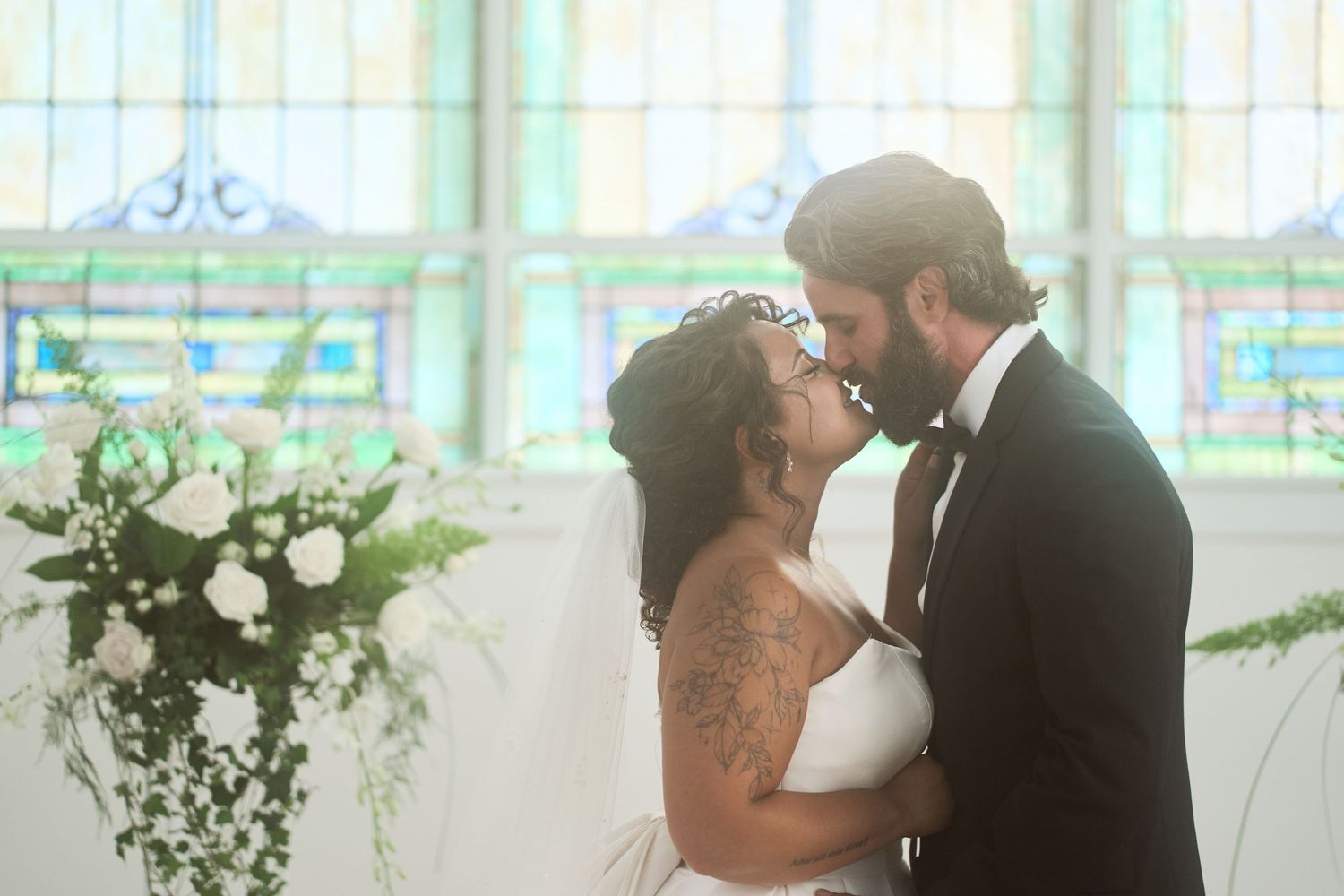Intimate wedding moment captured in front of gorgeous stained glass windows with natural light streaming in.
