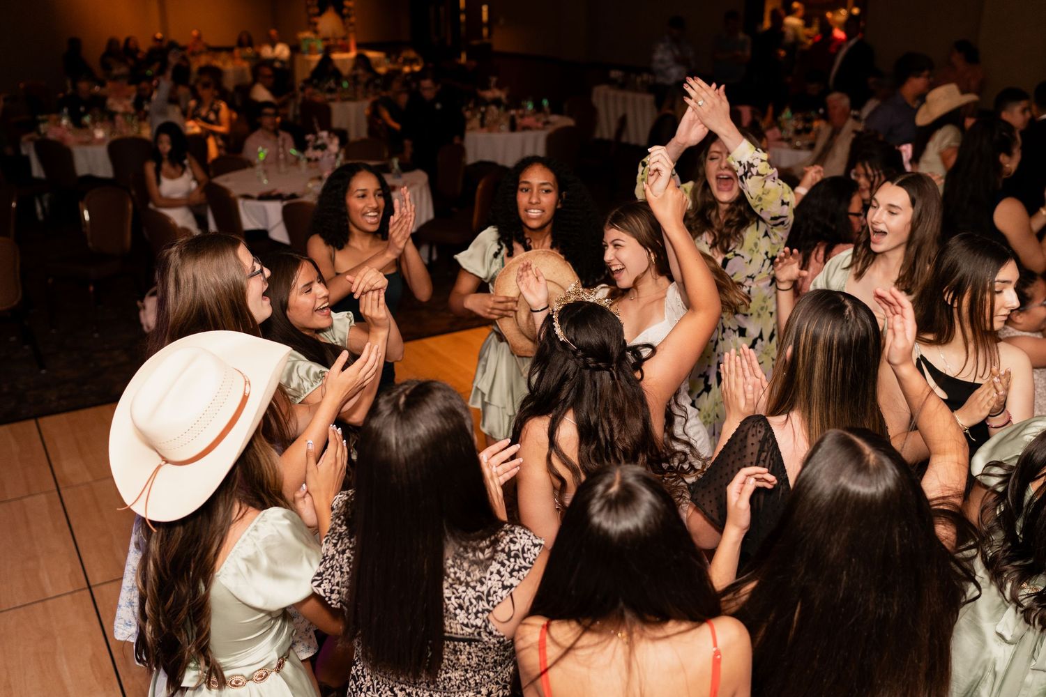 A lively crowd of party guests dance and celebrate on a dimly lit dance floor at an indoor event.