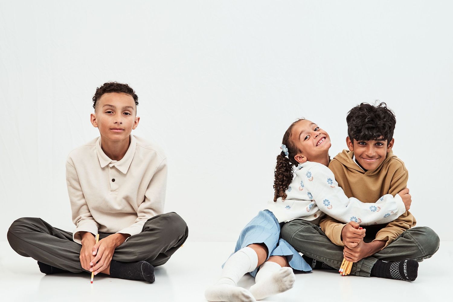 Three children sitting together on floor in casual clothing against white background.