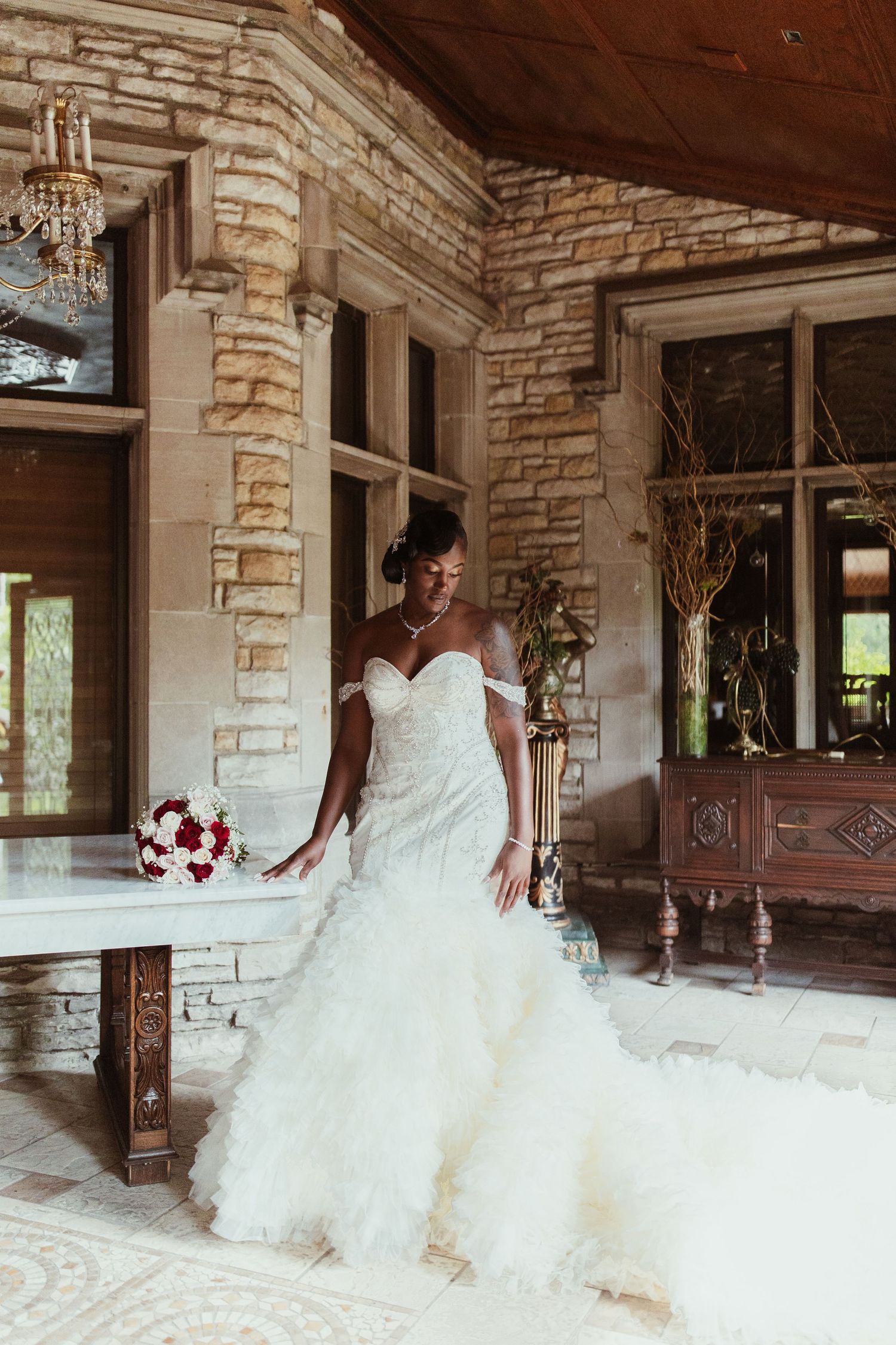 Stunning white mermaid wedding dress with sweetheart neckline and red bouquet in elegant stone venue.