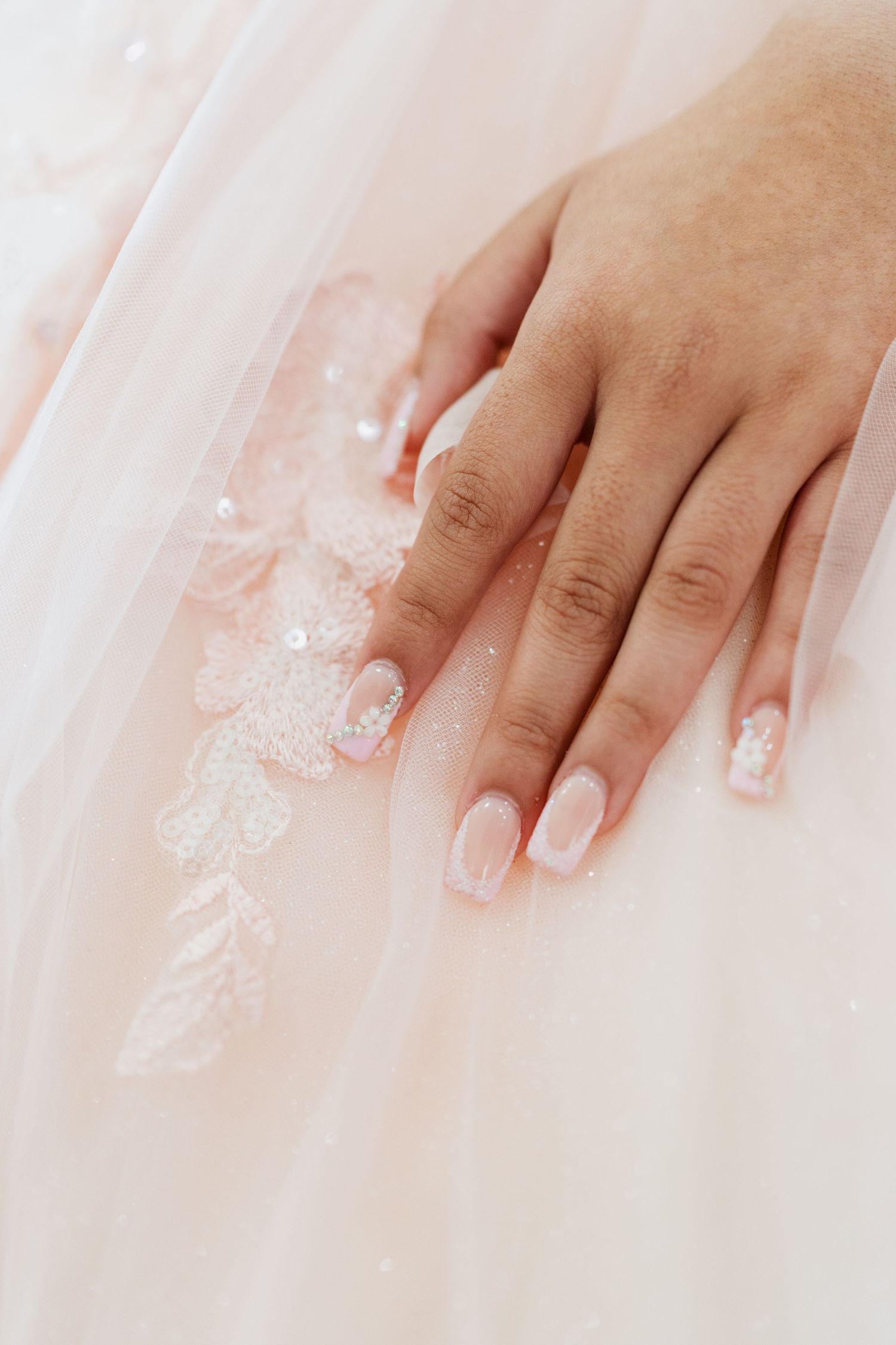 Close up view of manicured hands with french tip nails on white satin background showing wedding details.