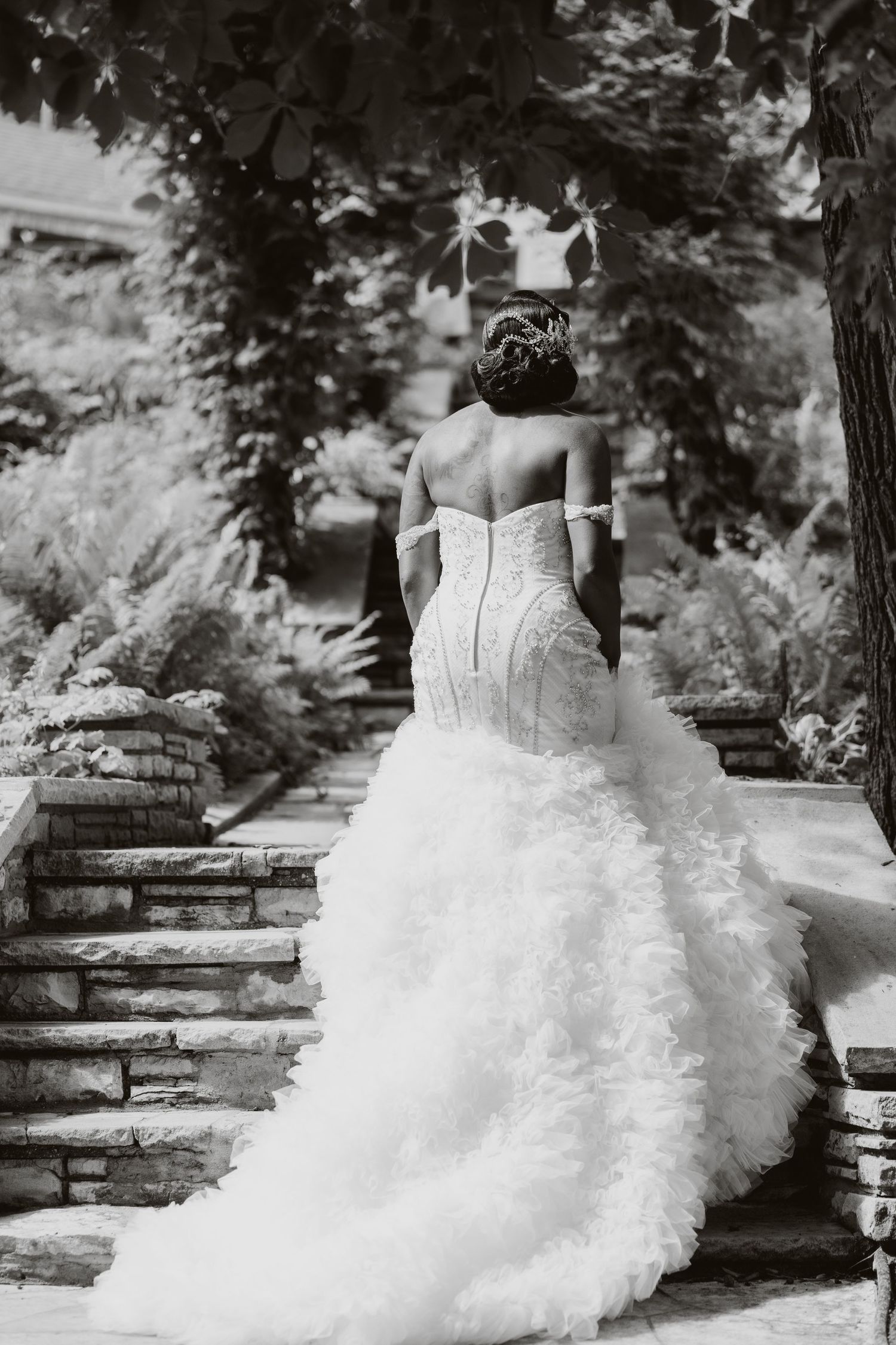 Stunning bridal gown with dramatic ruffled train photographed from behind on stone steps.