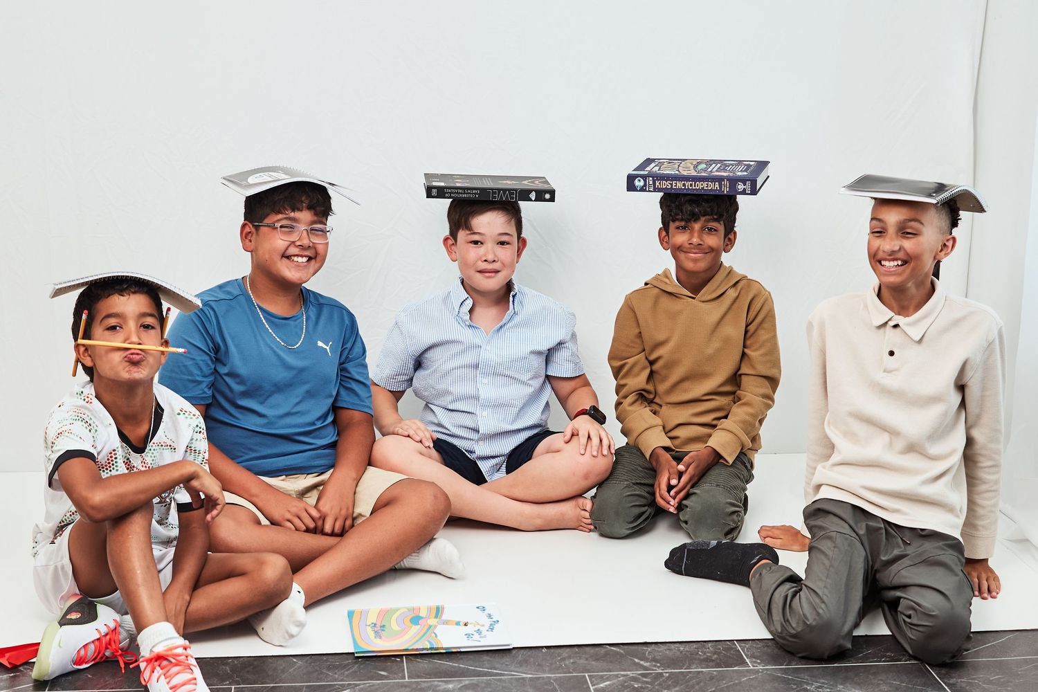 Five people sit together wearing textbooks on their heads while smiling at the camera.