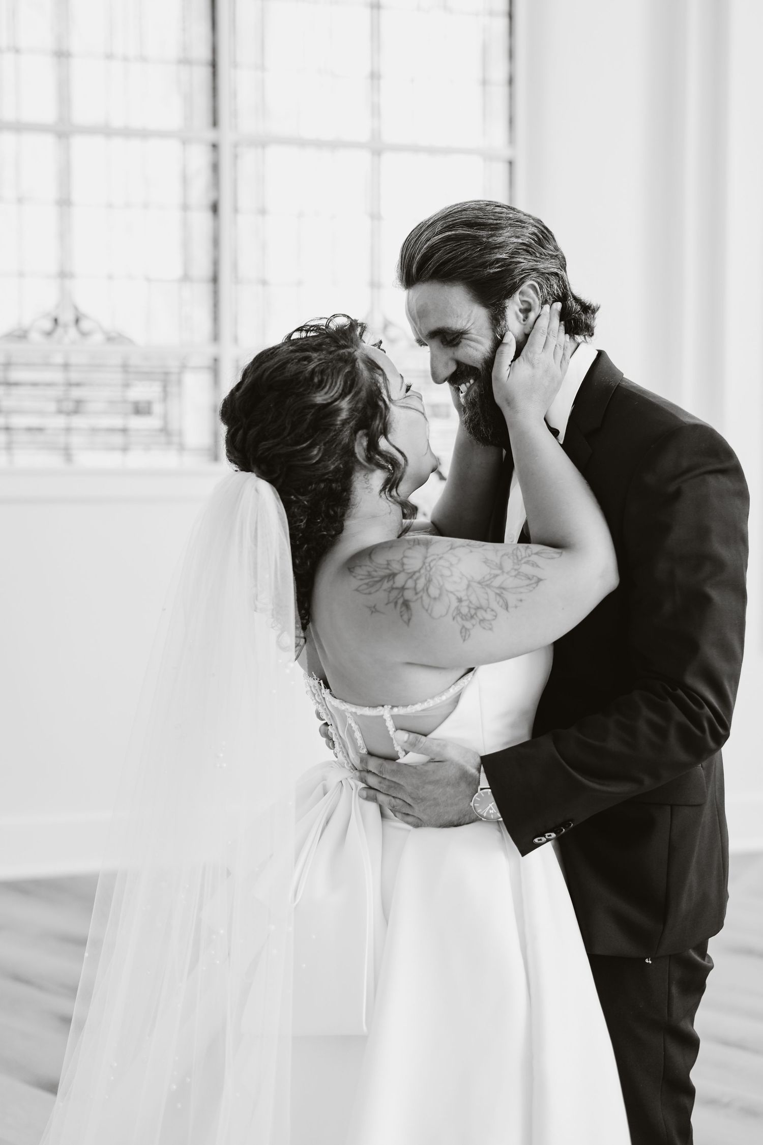 A romantic black and white wedding photo capturing a tender embrace between newlyweds in formal attire.