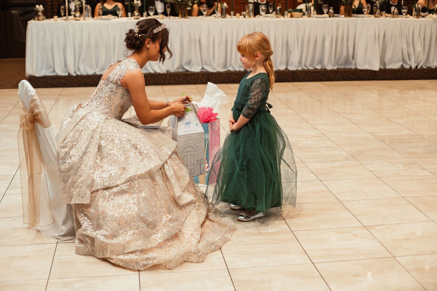 A magical moment as the bride in a glittering gown interacts with a small child in green at the reception.