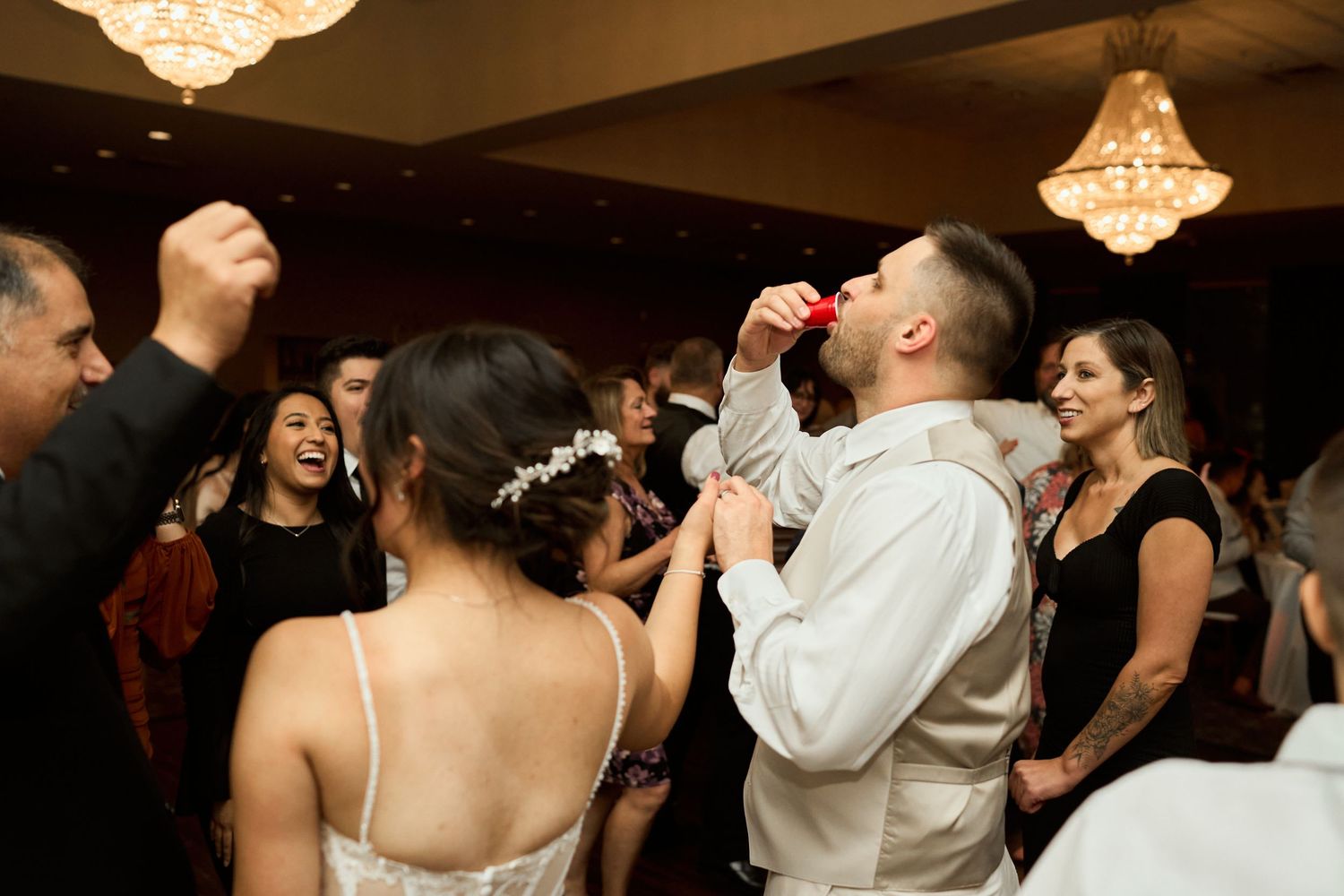 Wedding guests dancing and celebrating on the dance floor under crystal chandeliers at an elegant reception venue.