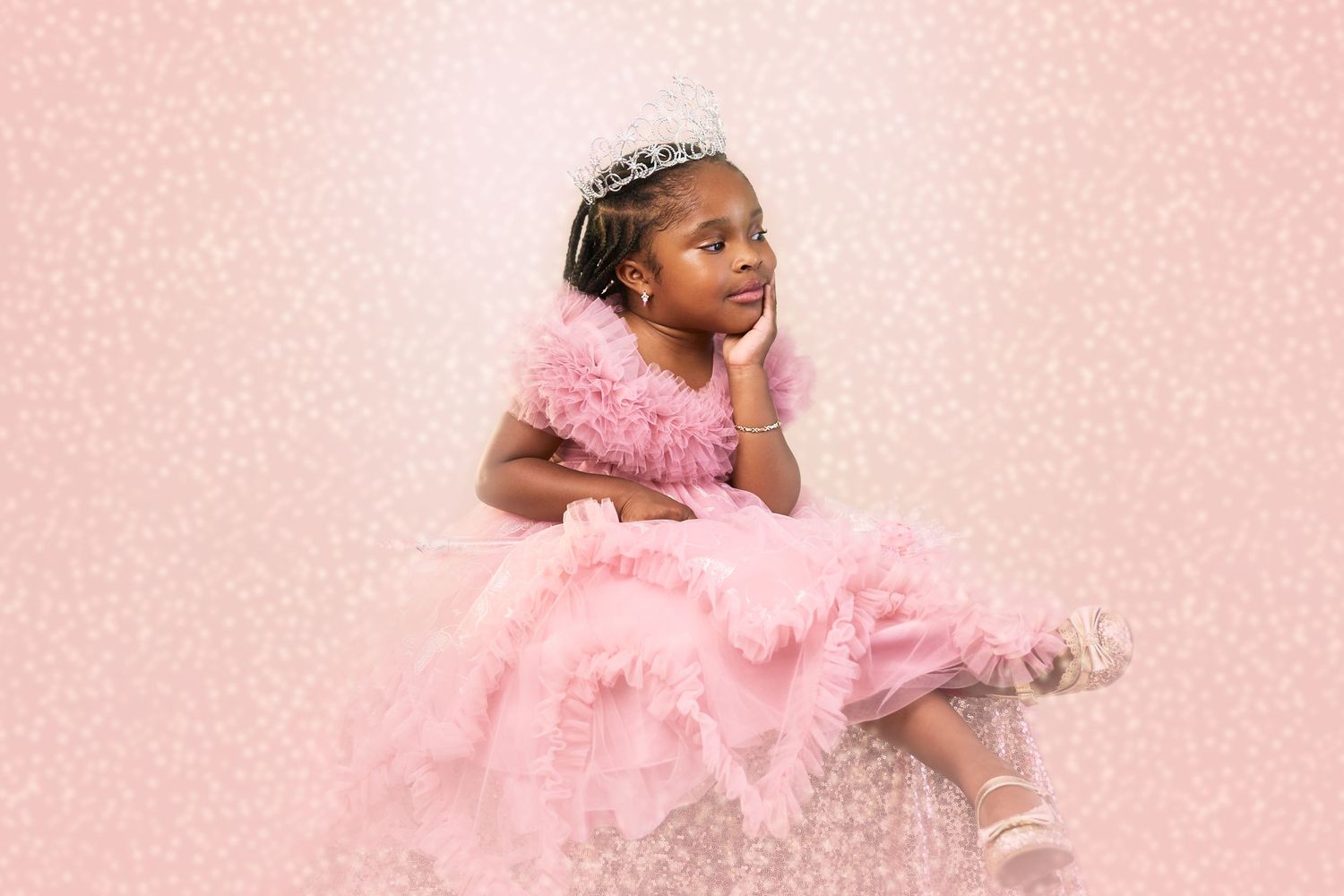 A young child in a pink tulle princess dress and tiara poses gracefully against a pink background.
