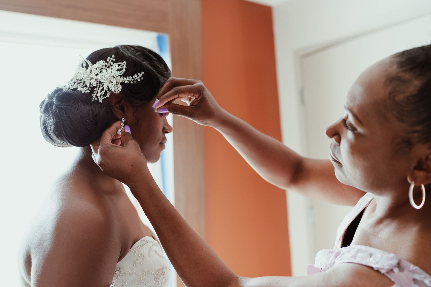 Final touches being made to bridal accessories against an orange wall.