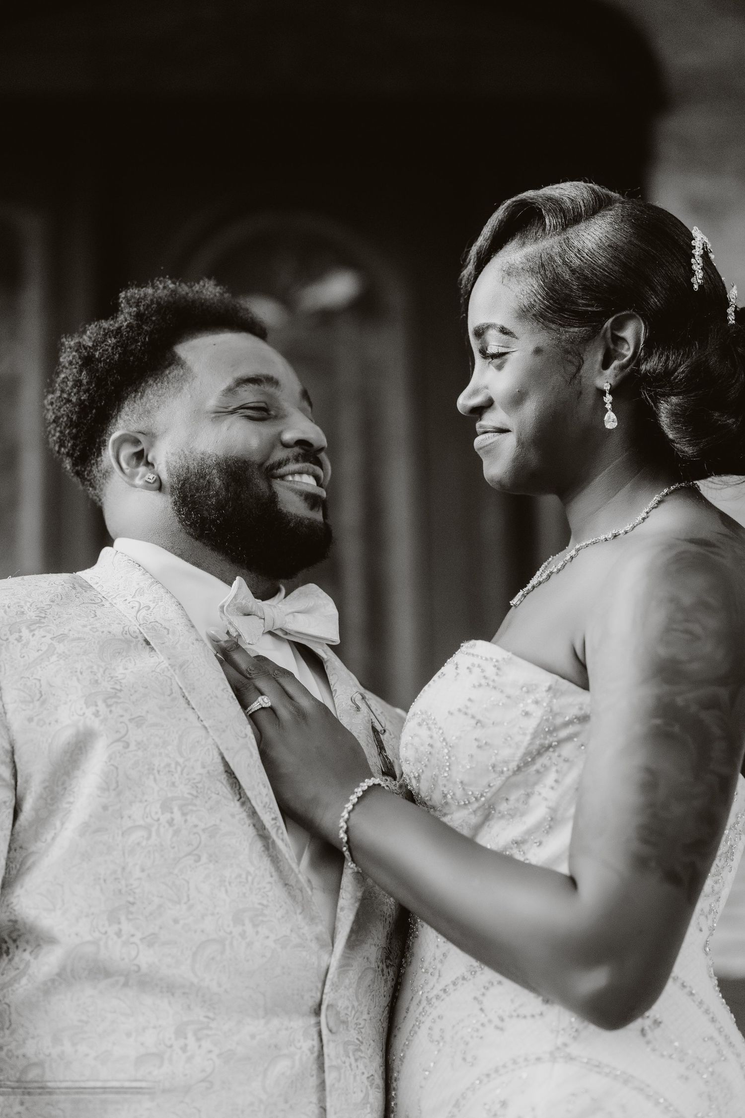A romantic black and white wedding portrait showing a tender moment between newlyweds in formal attire.